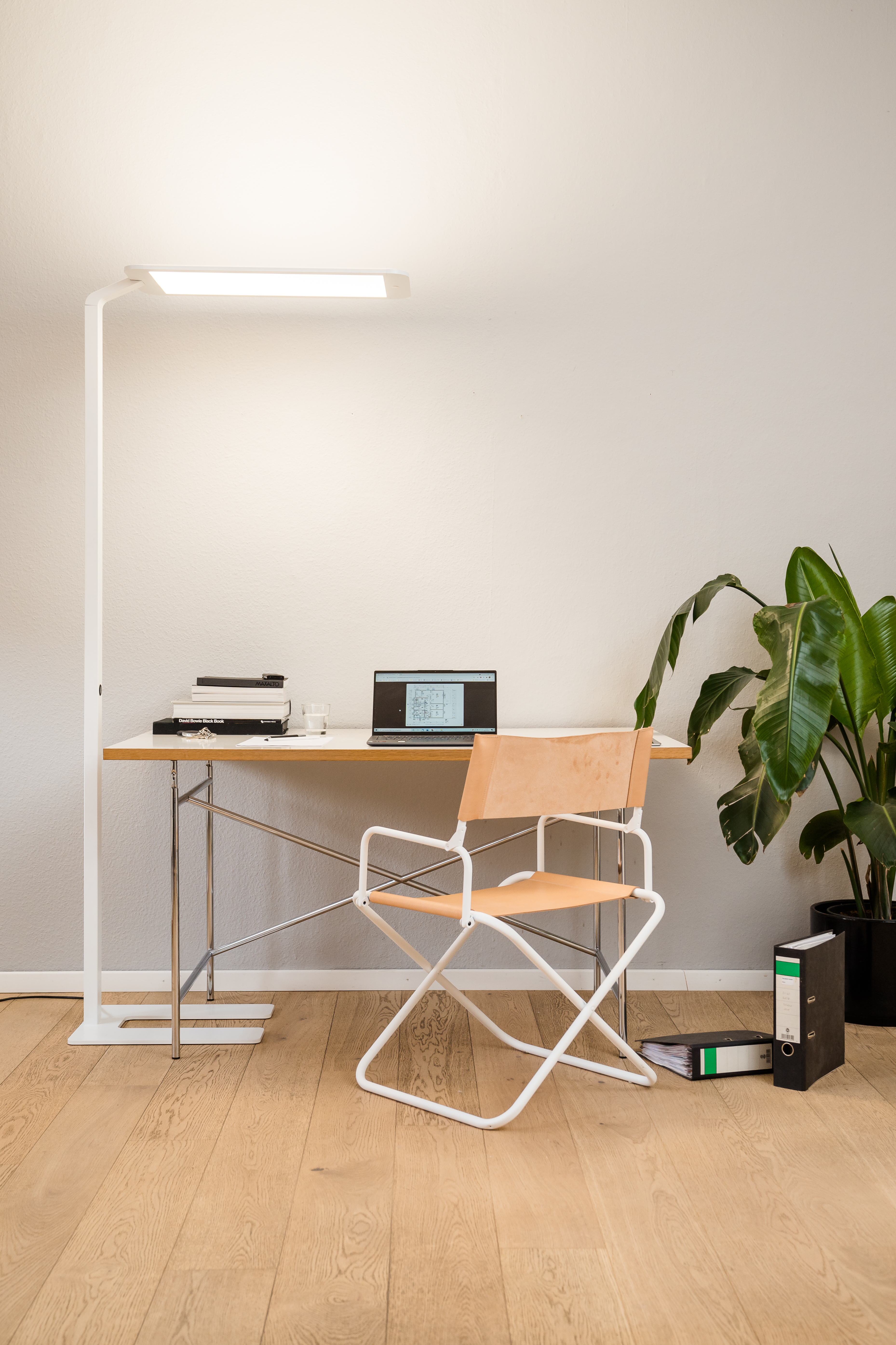 Büro mit Stehlampe, Schreibtisch, Stuhl und Laptop.