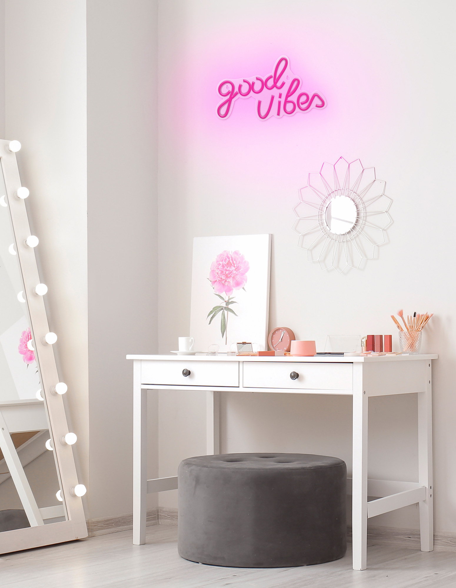 Una toeletta con specchio, un'insegna al neon rosa con la scritta 'good vibes' e trucco sulla scrivania.