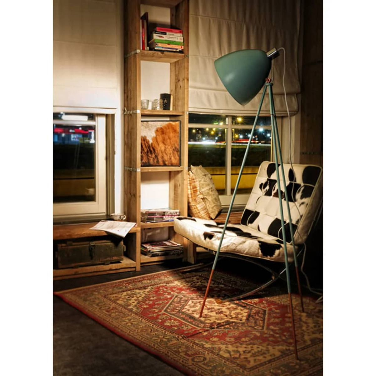 Una habitación con una silla, una alfombra, una estantería de madera y una lámpara con pantalla azul.