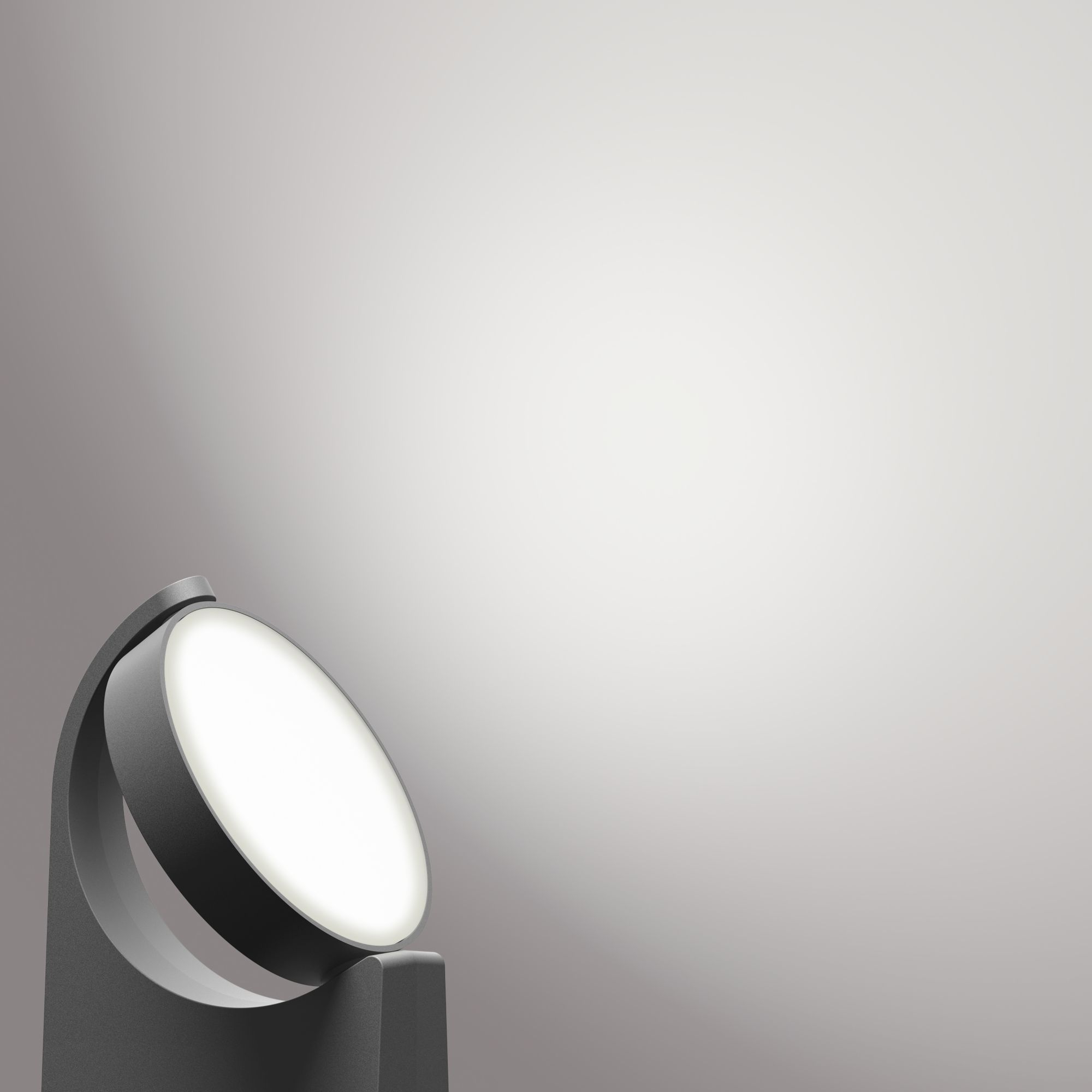 Faretto grigio moderno inclinato verso destra, che emette luce intensa su una superficie grigio chiaro.
