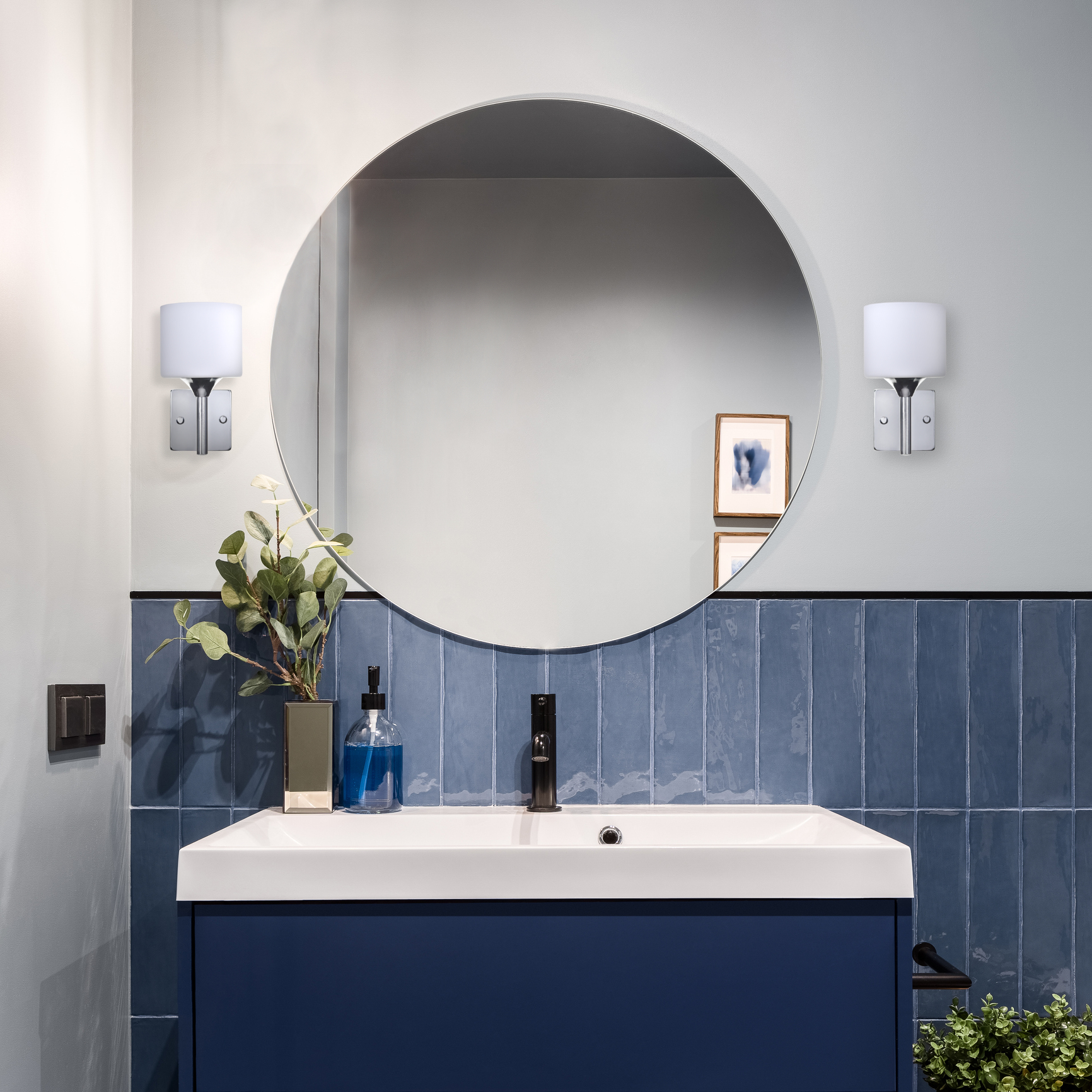 Scena łazienkowa z lustrem, dwiema lampami ściennymi, umywalką i niebieską szafką.