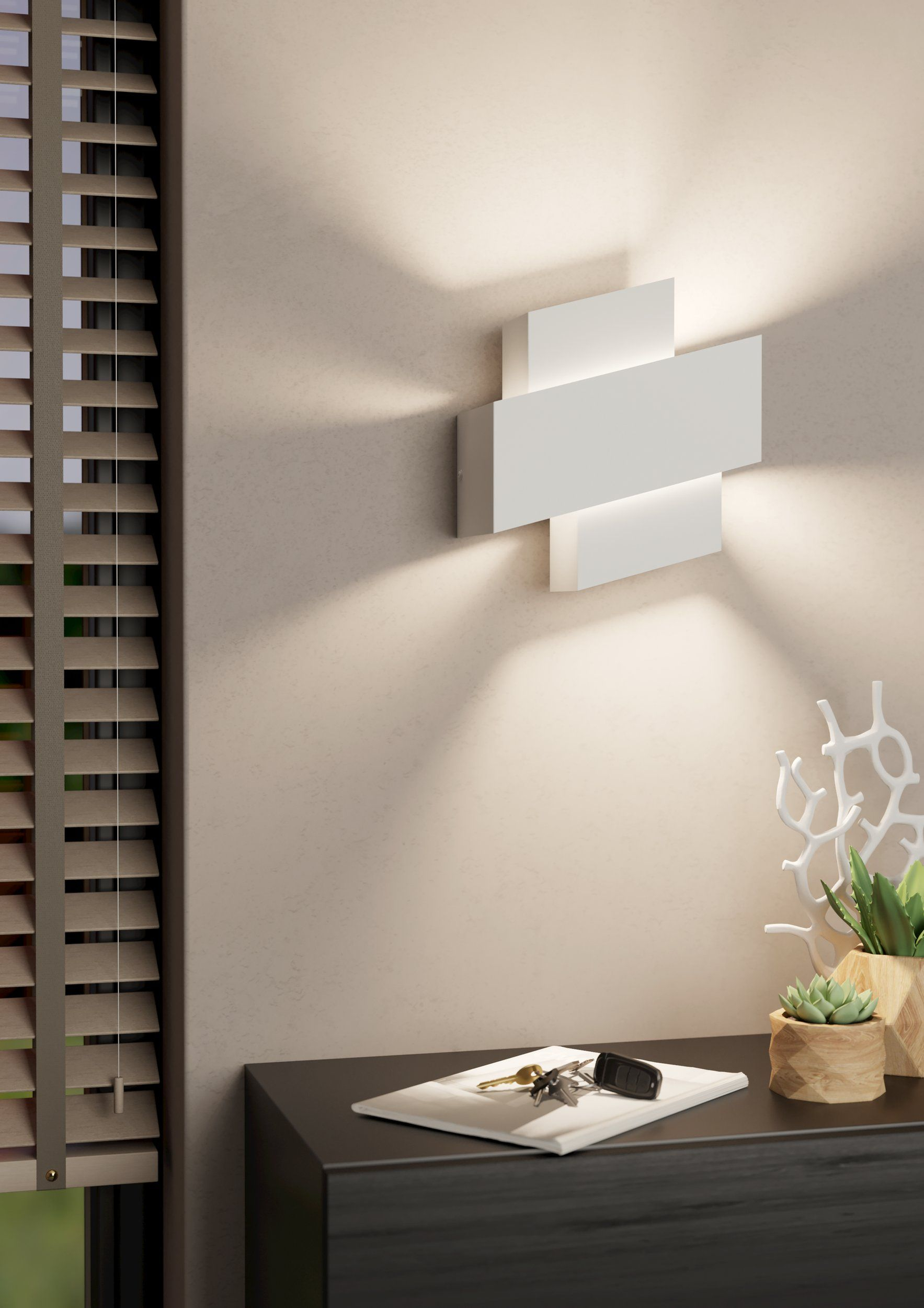 Weiße Wandleuchte im Kreuz-Design, wirft Licht auf eine beige Wand. Schlüssel und Notizbuch auf einer Oberfläche.