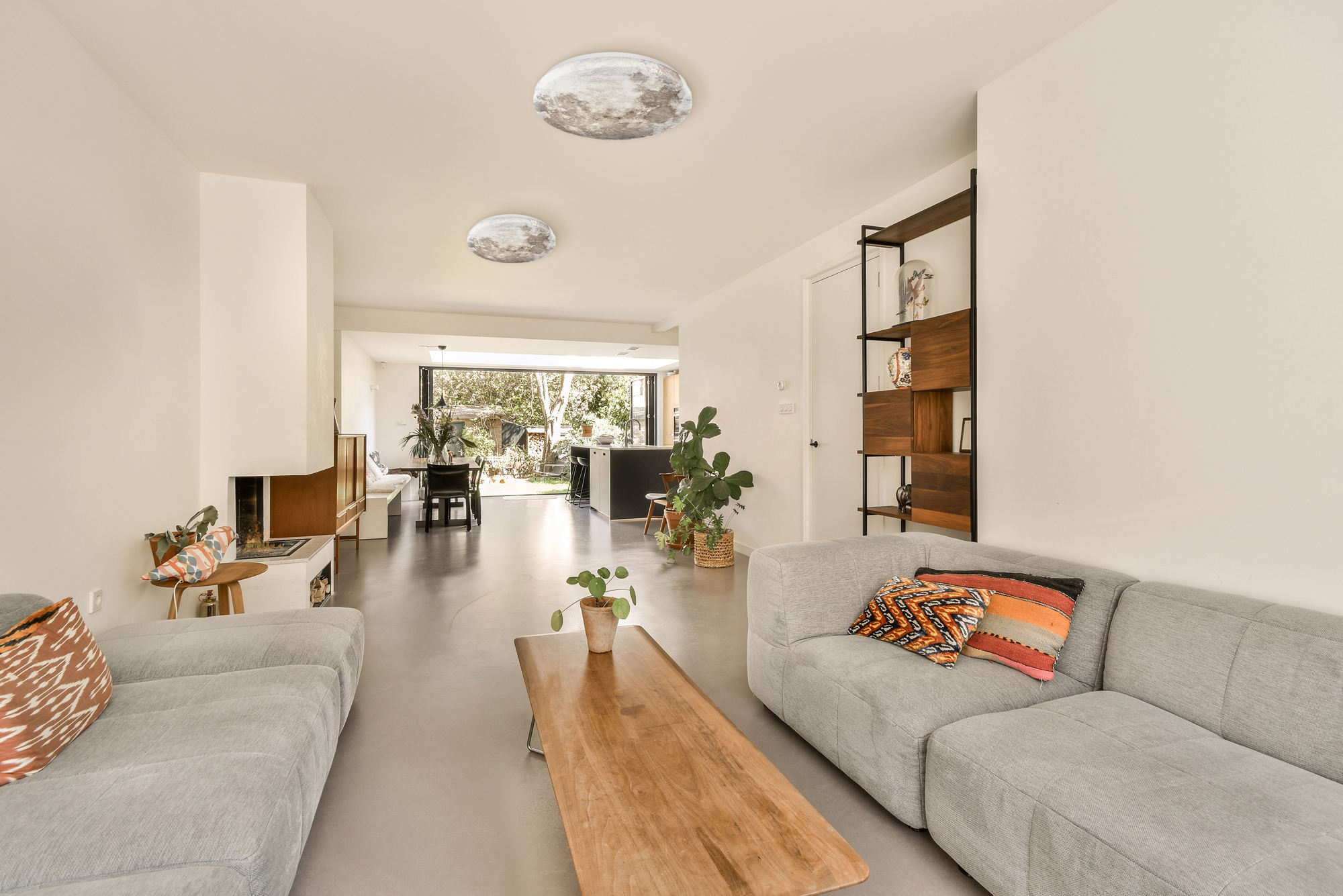 Nowoczesny salon z szarymi sofami, drewnianym stołem i dwoma lampami sufitowymi w kształcie księżyca.