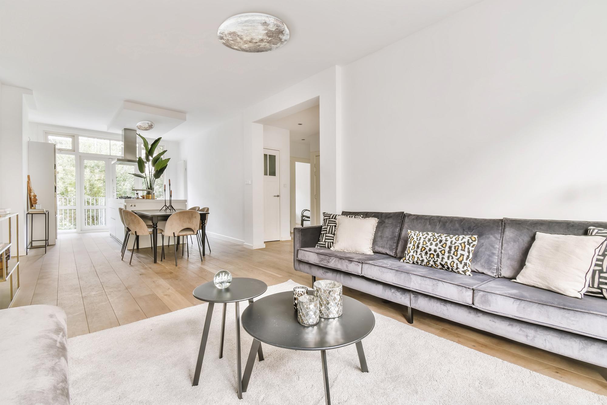 Salon z szarą sofą, stolikami kawowymi, dywanem i jadalnią w tle.