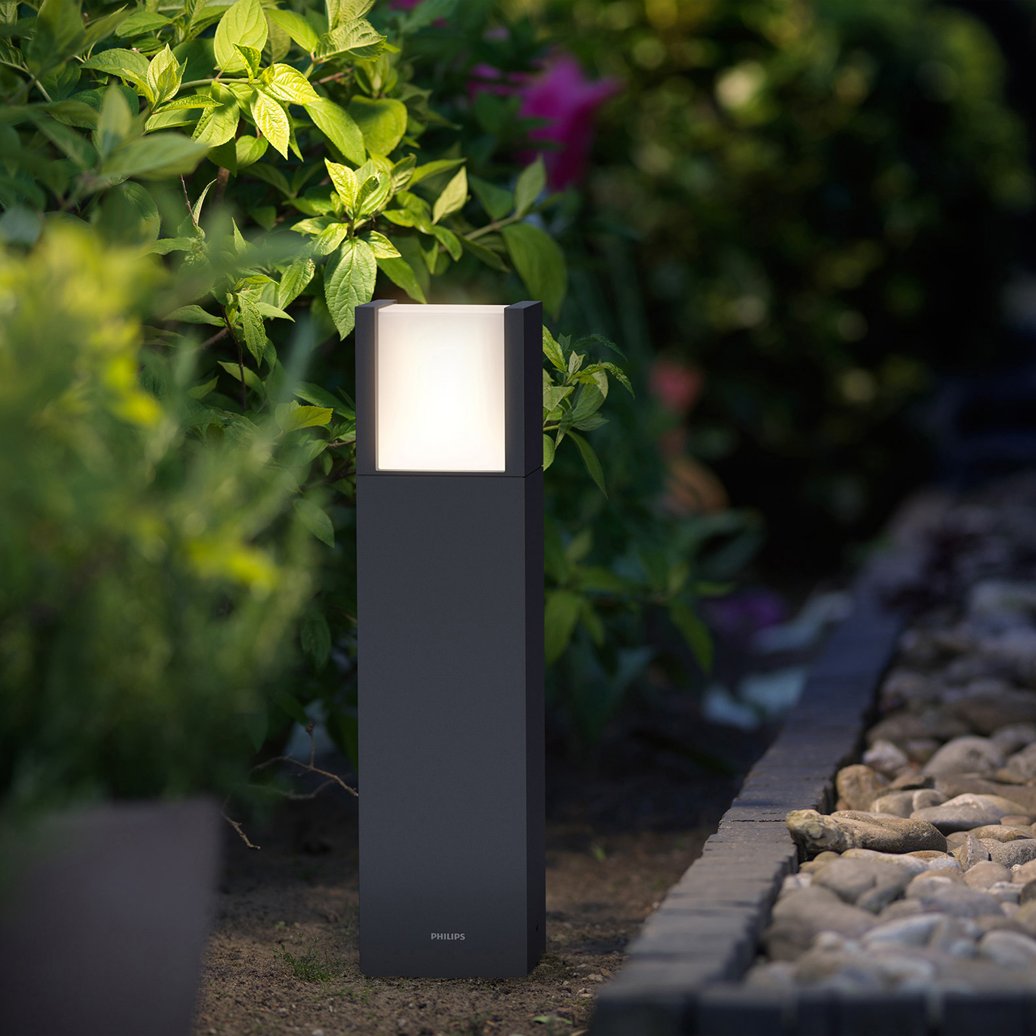Luce a colonna LED nera per esterni, design rettangolare, illuminata, in un giardino con piante.