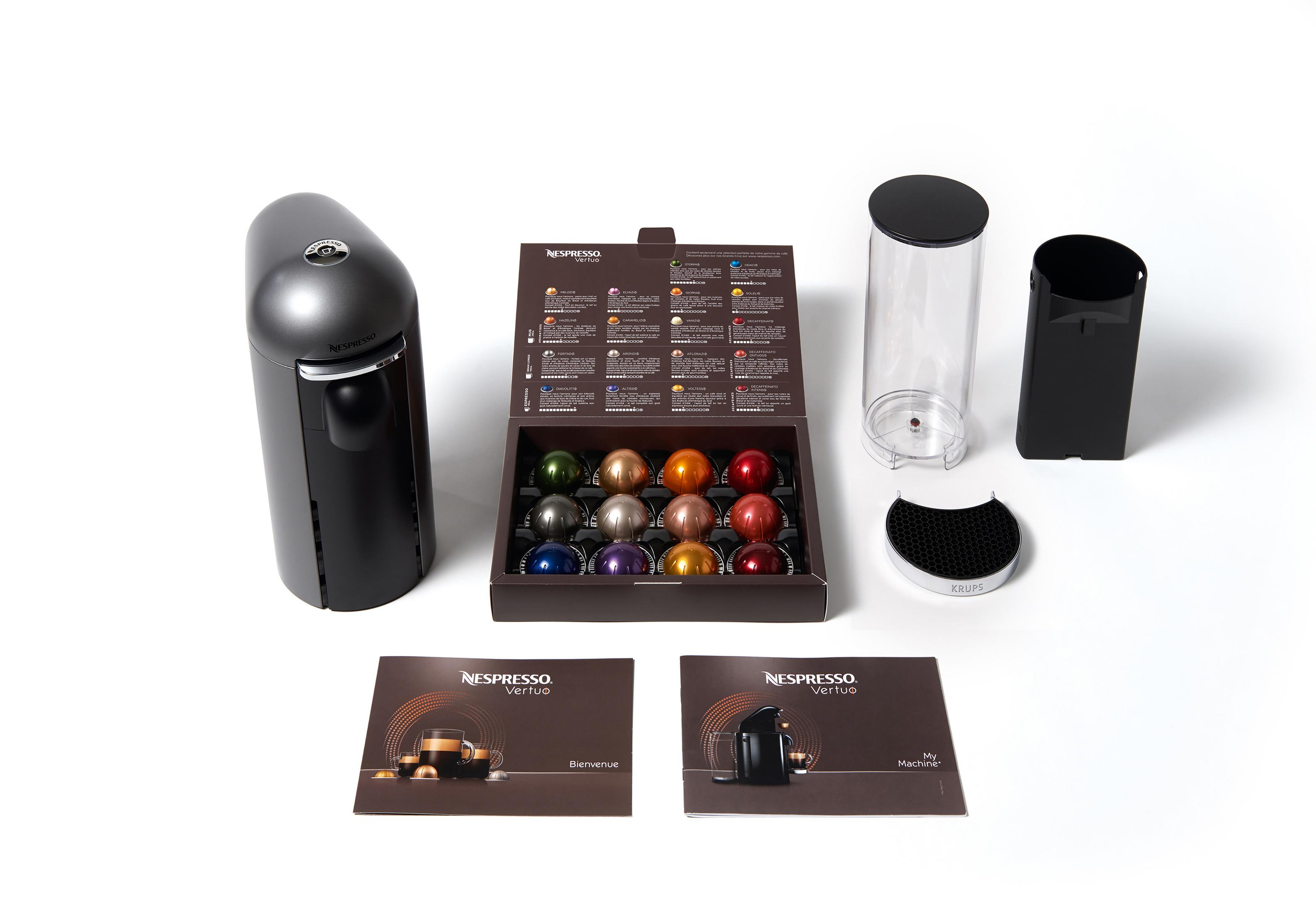 Nespresso Vertuo Kaffeemaschine mit Kapseln, Zubehör und Broschüren auf Weiß.