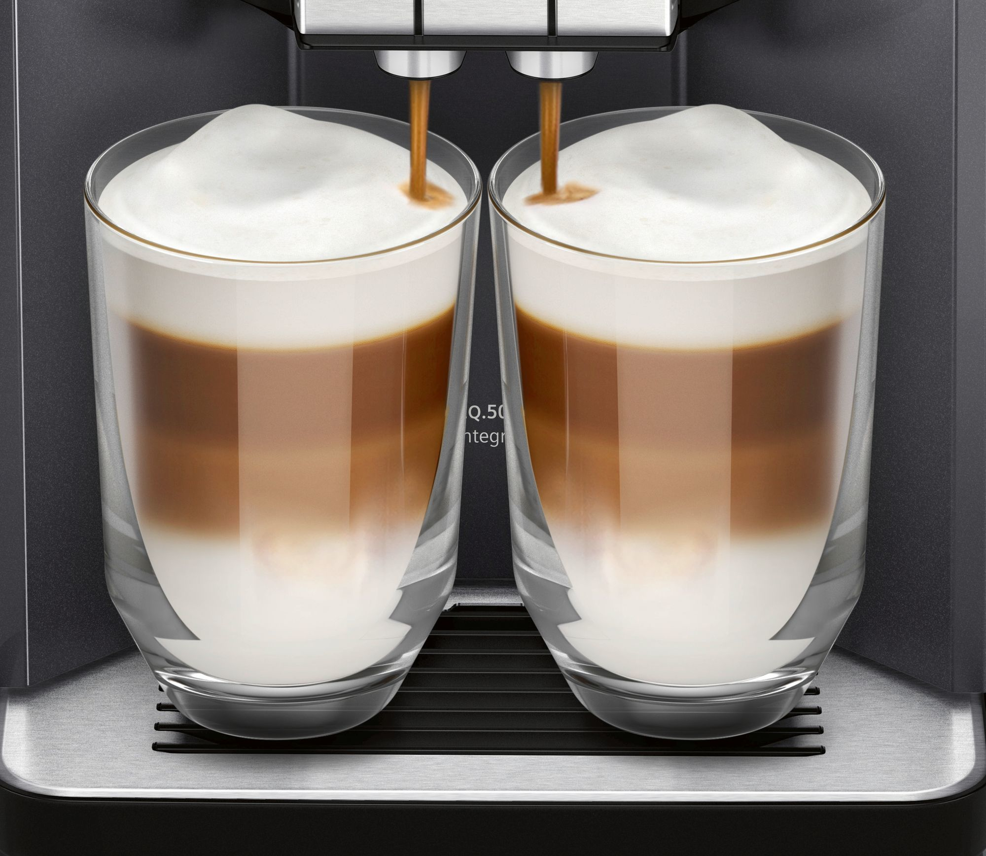 Zwei Gläser mit geschichteten Kaffeegetränken, die von einer Kaffeemaschine gefüllt werden. Schaum bedeckt die Getränke.