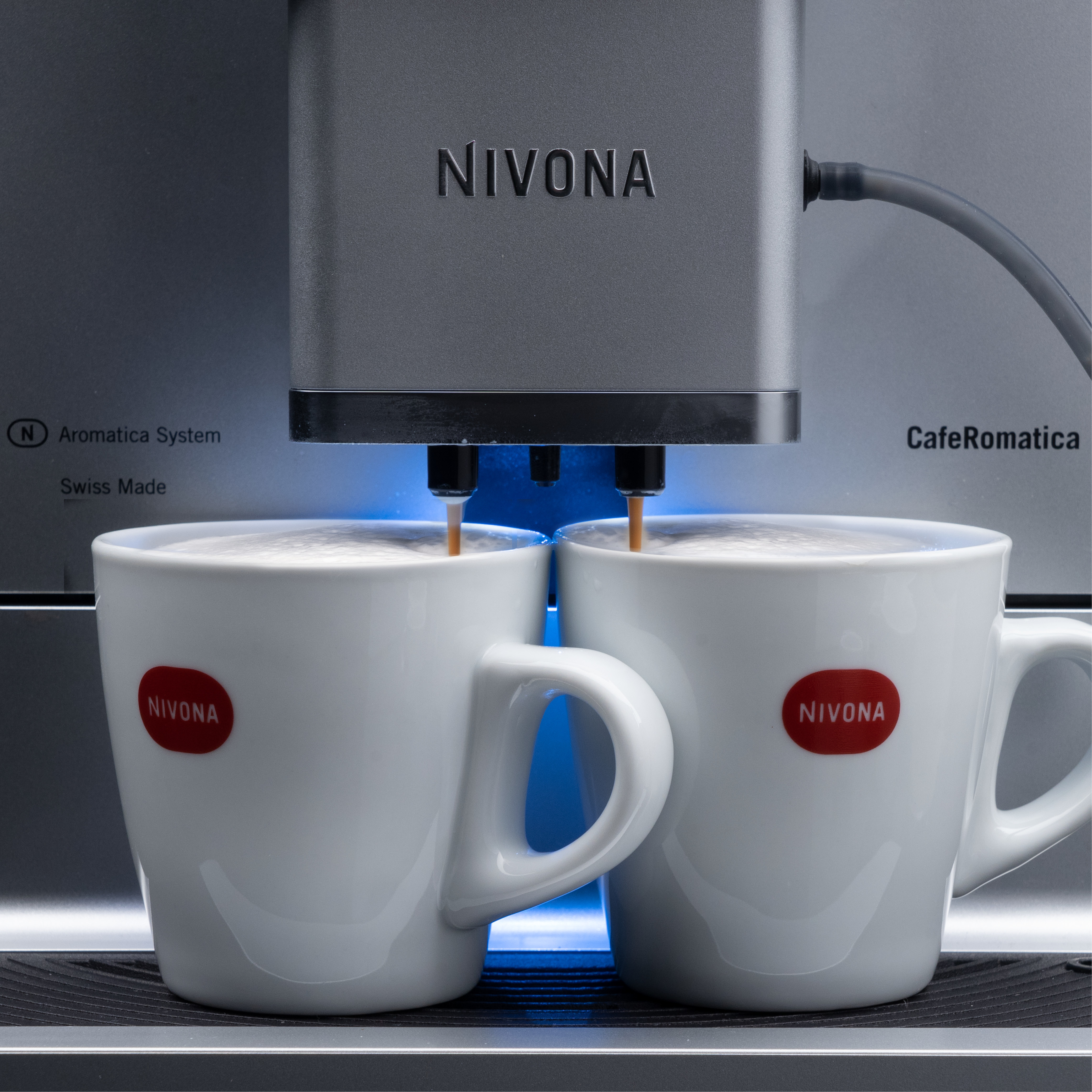 Macchina da caffè che eroga caffè in due tazze bianche con logo.