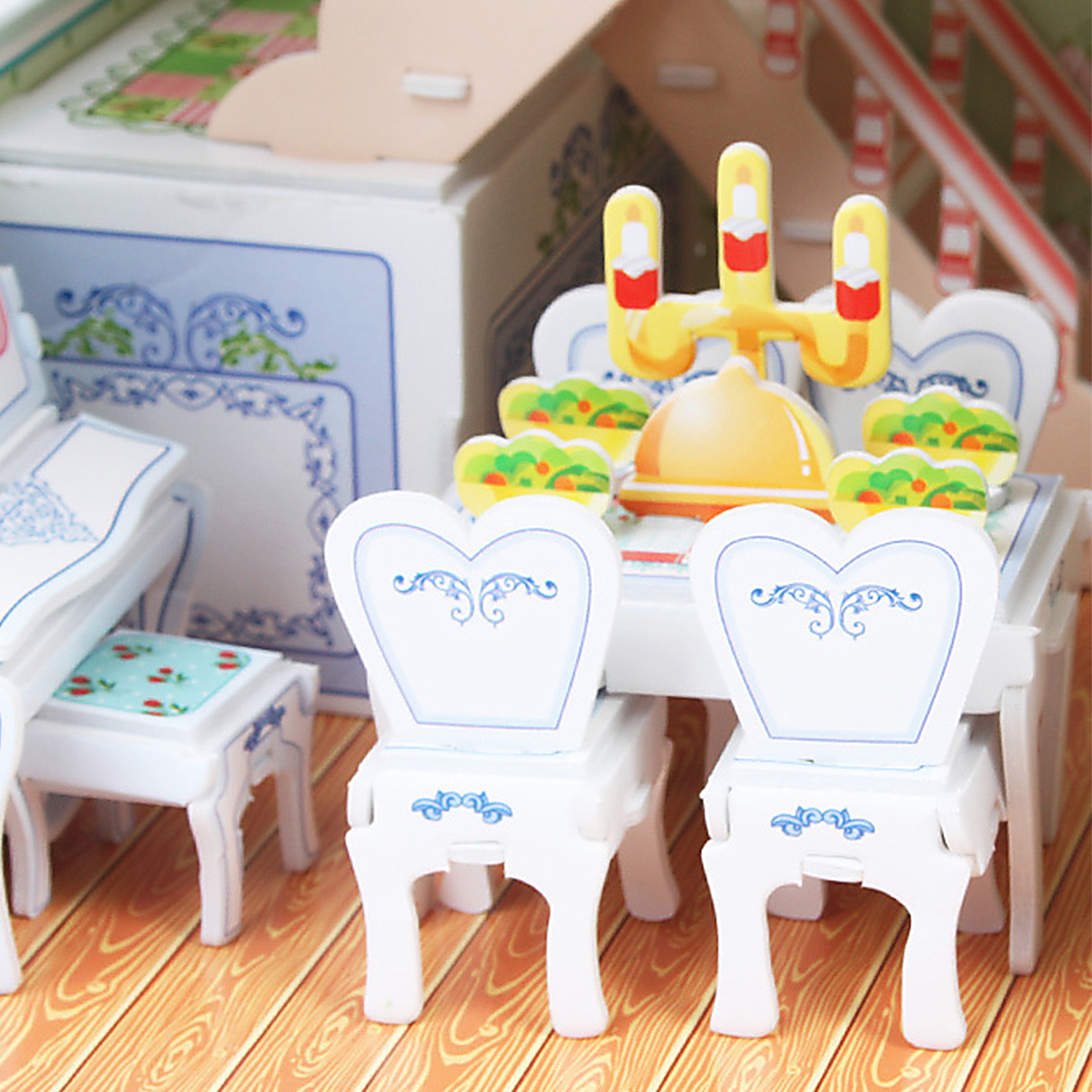 Un set da sala da pranzo per casa delle bambole con tavolo, sedie e stoviglie decorative, su sfondo bianco.