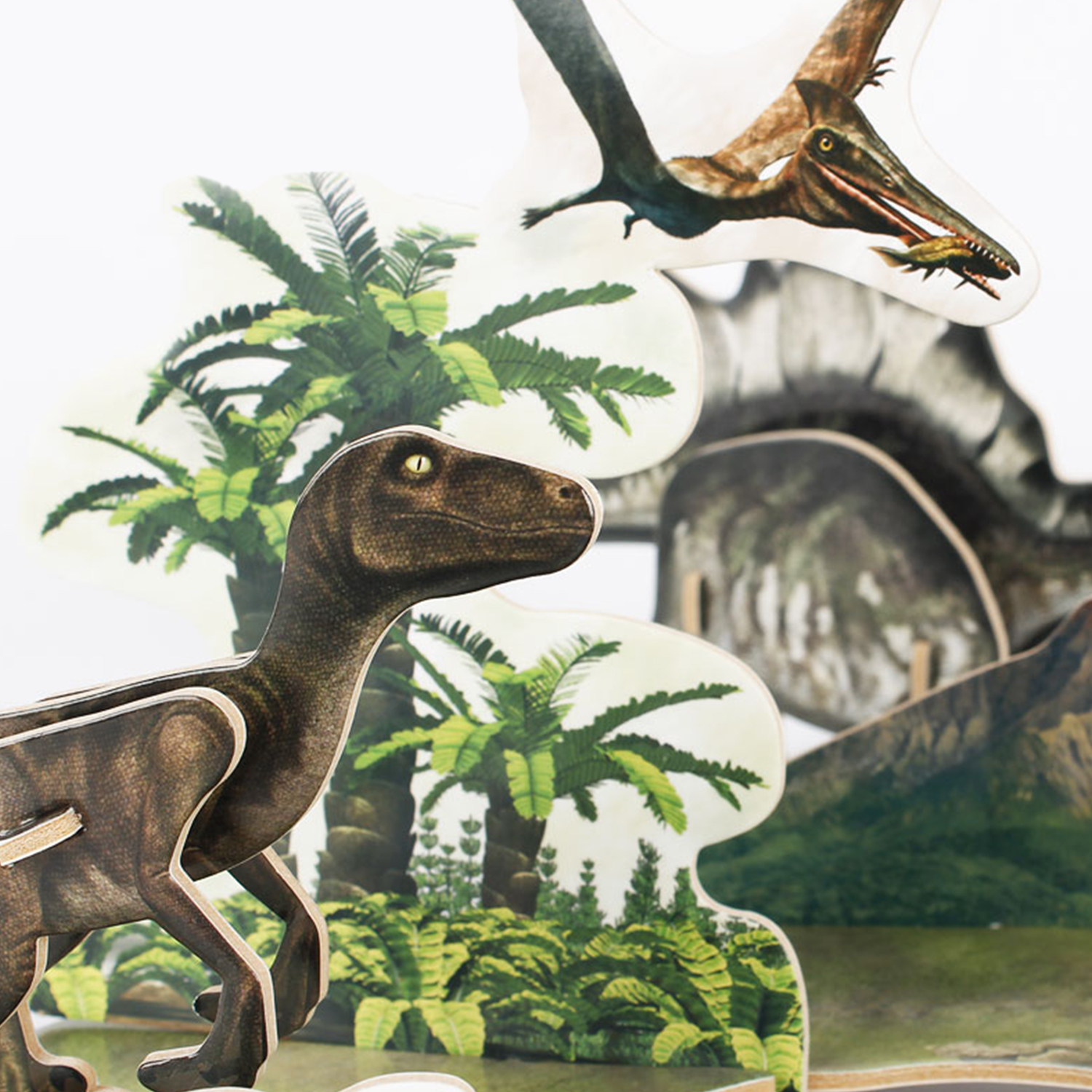 Una escena de dinosaurios 3D con un raptor, pterodáctilo, palmeras y un fondo montañoso.