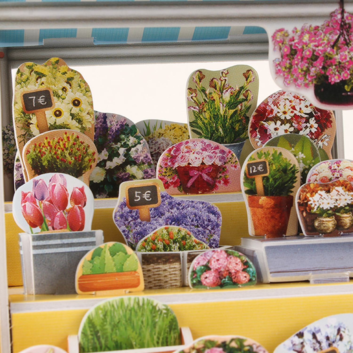 Ein Miniatur-Blumenladen mit verschiedenen Blumen und Preisschildern. Eine blau-weiß gestreifte Markise.
