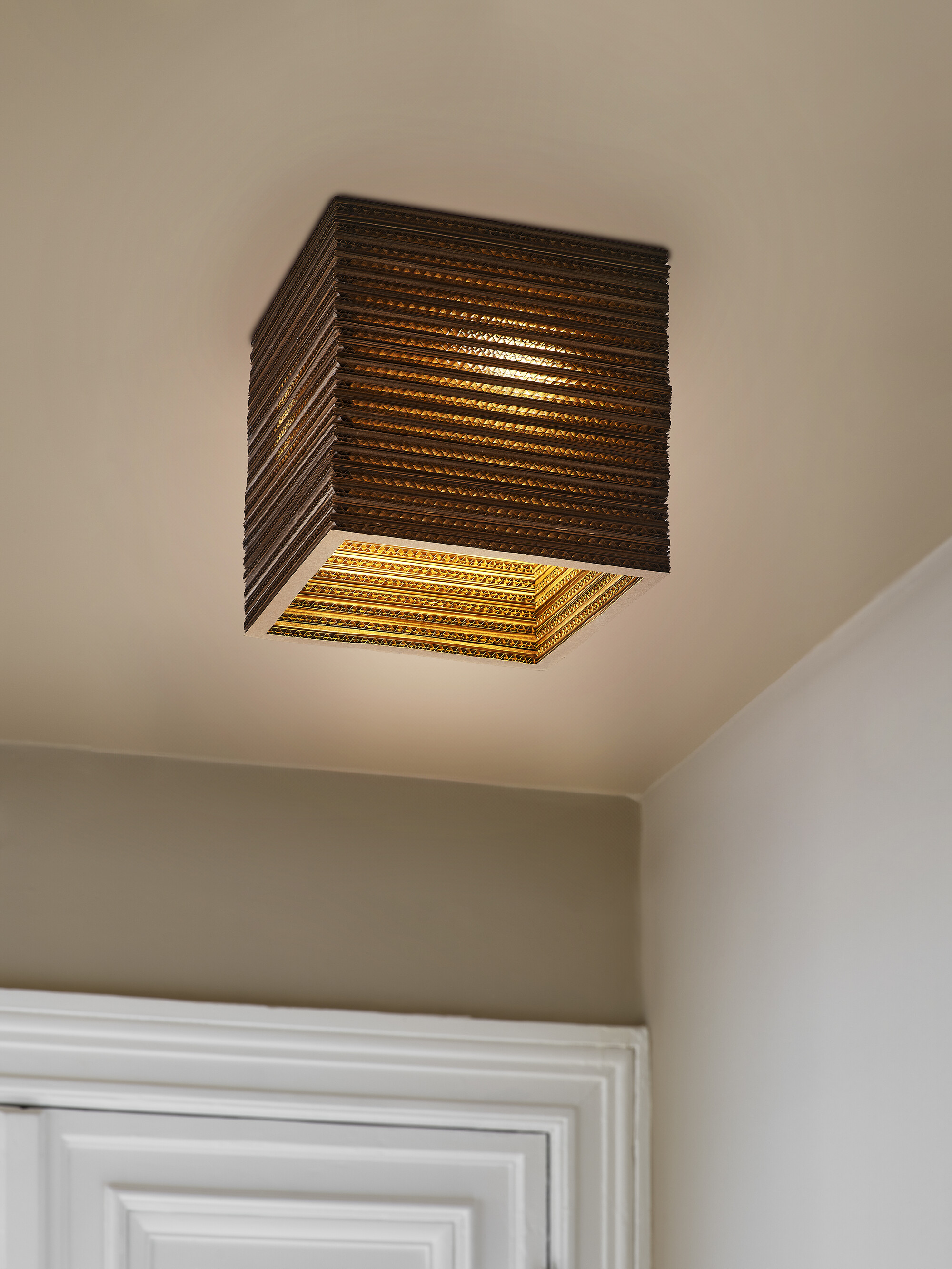 Eine quadratische Lampe aus Wellpappe, die von der Decke hängt.
