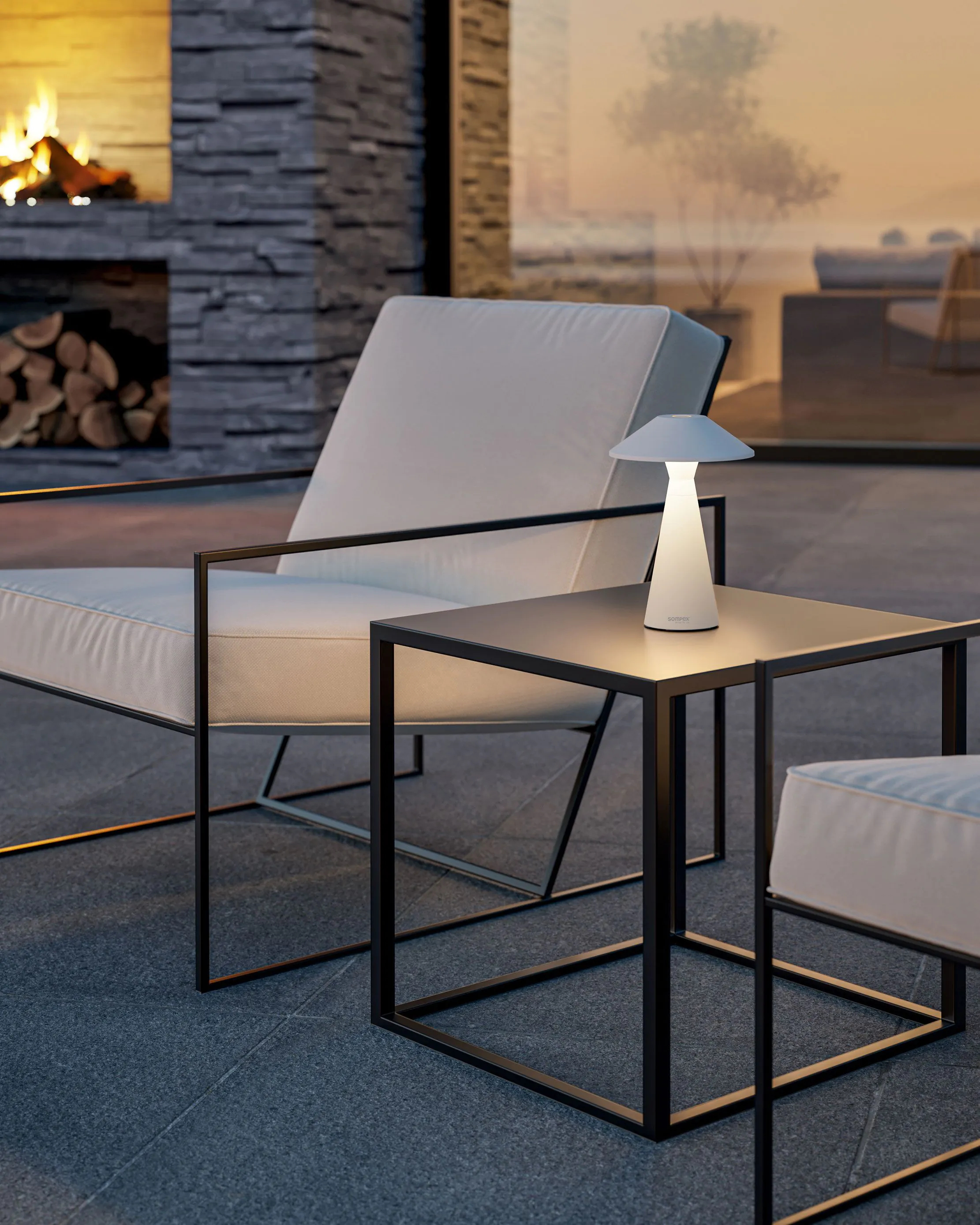Biała lampa na czarnym stoliku, krzesło i tło patio z kominkiem.