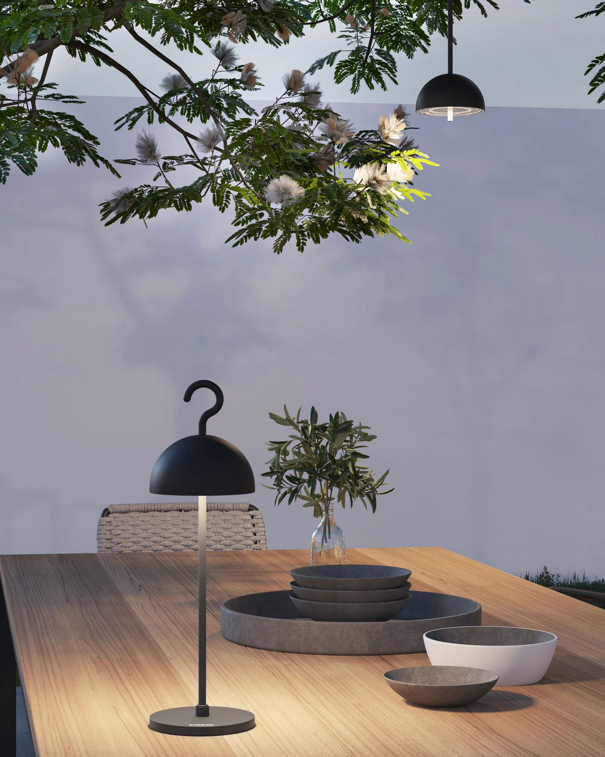 Stół do spożywania posiłków na świeżym powietrzu z czarną lampą i innymi dekoracjami pod drzewem.