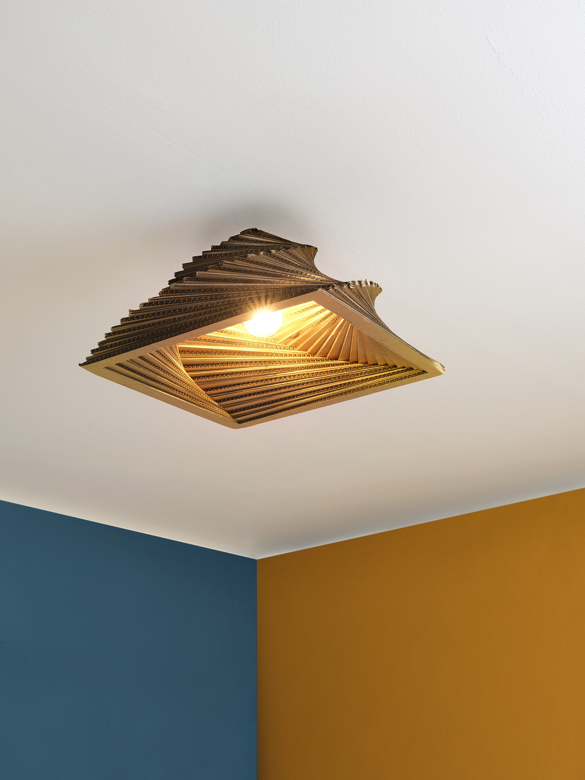 Deckenlampe mit geschichtetem, quadratischem Design, sichtbare Glühbirne, vor weißer Decke.