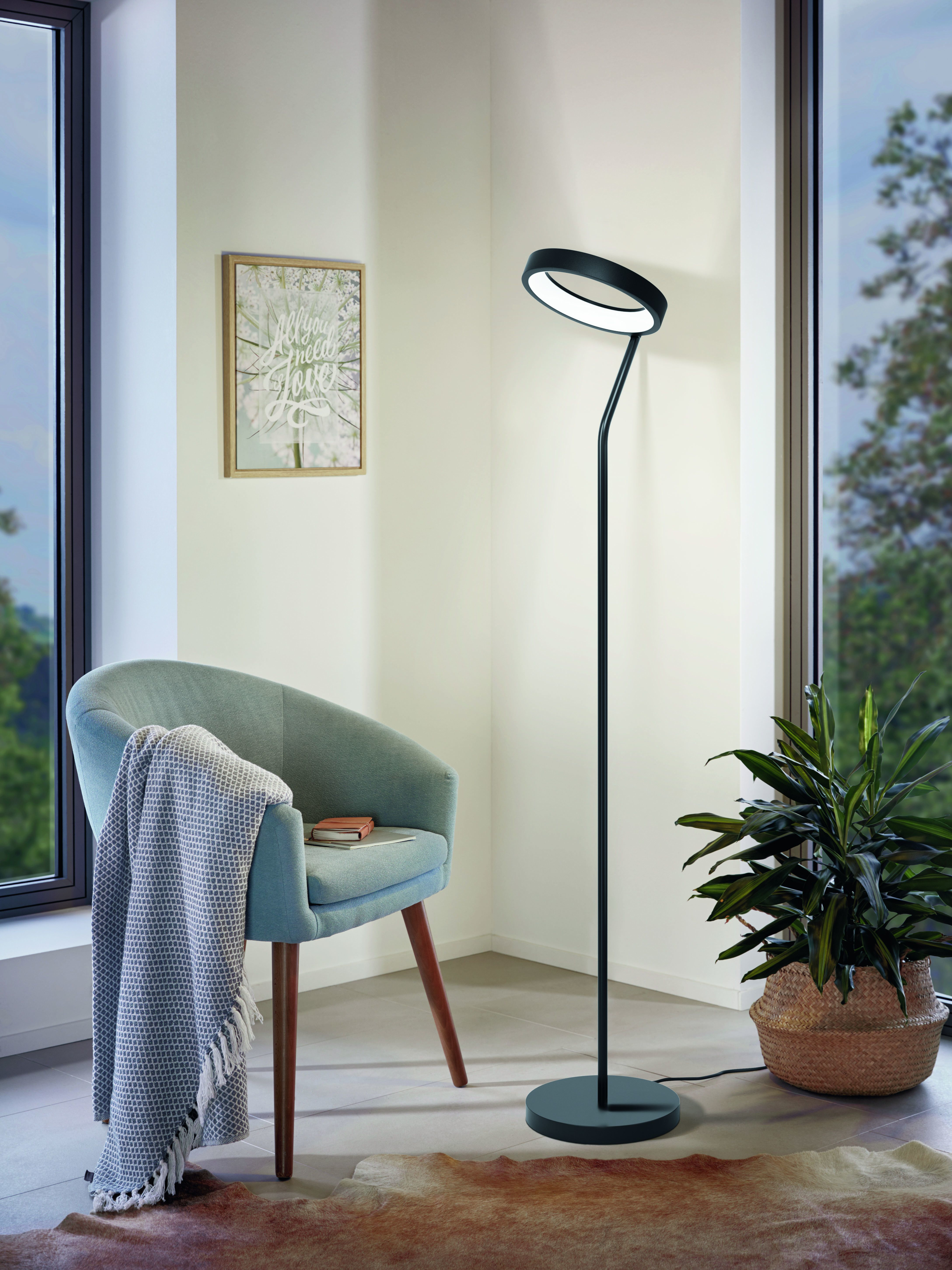Moderne Stehlampe mit rundem Kopf, neben Stuhl und Pflanze.