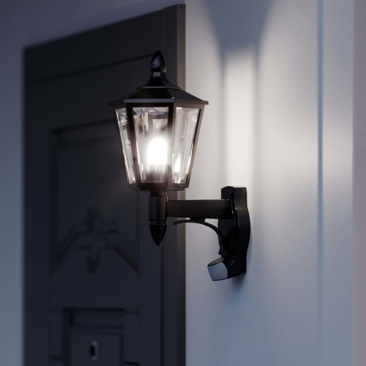 Schwarze Außenwandleuchte an einer Wand, Licht scheint, eine Tür im dunklen Hintergrund, bei Nacht.
