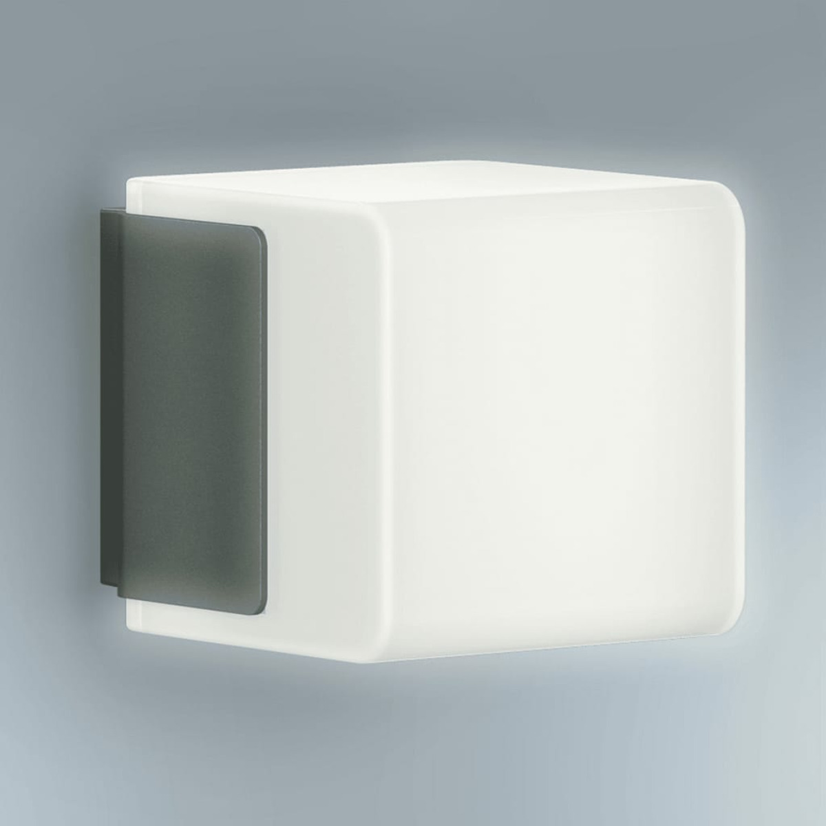 Lampada da parete bianca a forma di cubo con pannello laterale grigio scuro, montata su sfondo grigio chiaro.