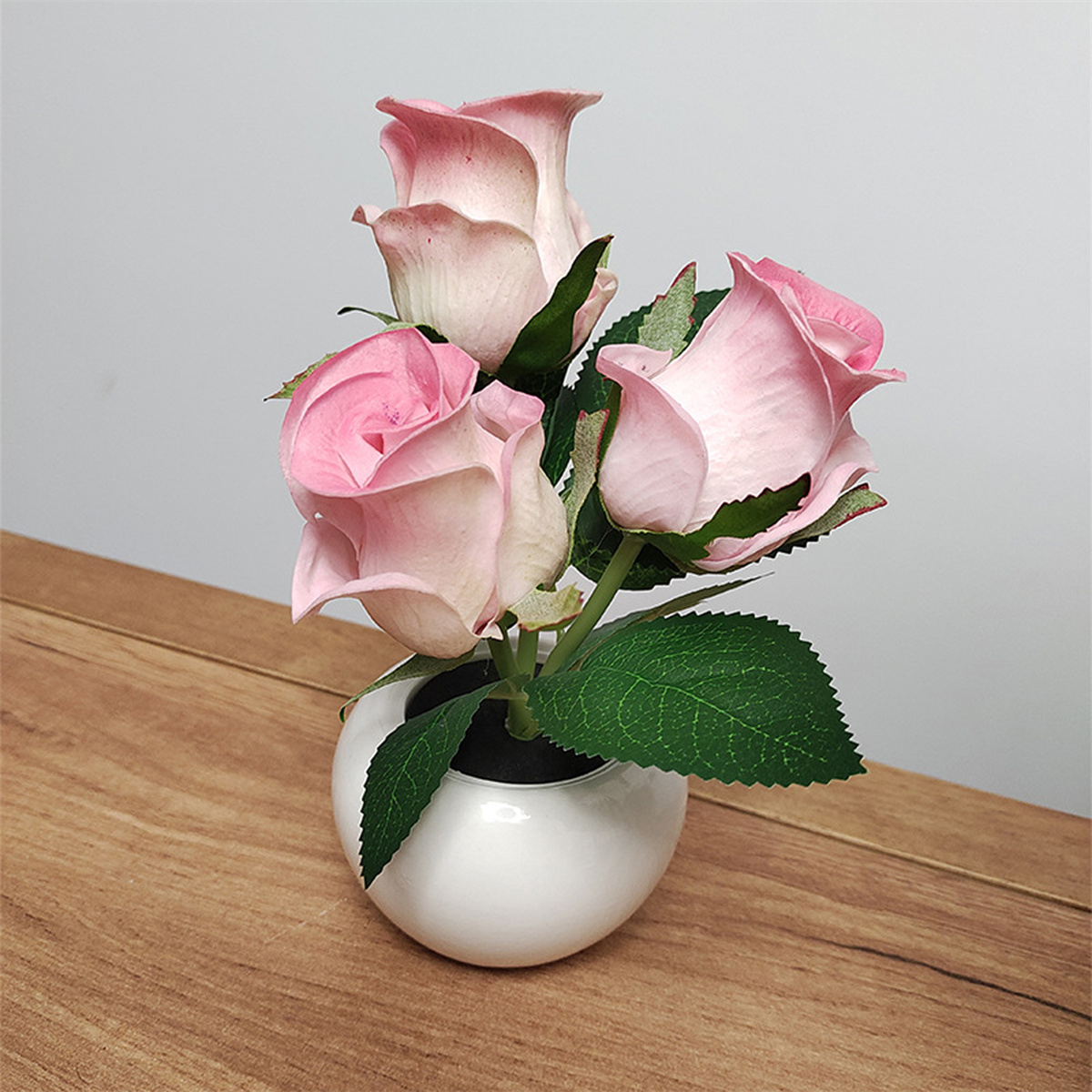 Drei rosa Rosen in einem weißen Keramiktopf auf einer Holzoberfläche.