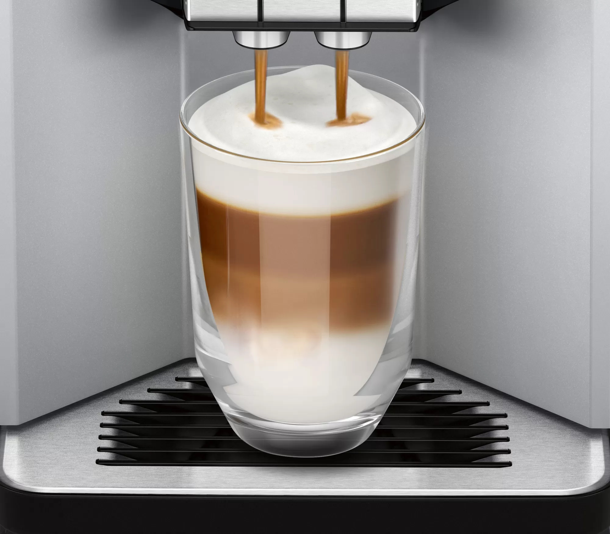 Kaffeemaschine, die Latte in ein Glas ausgibt. Schichten aus Schaum und Kaffee sind sichtbar.