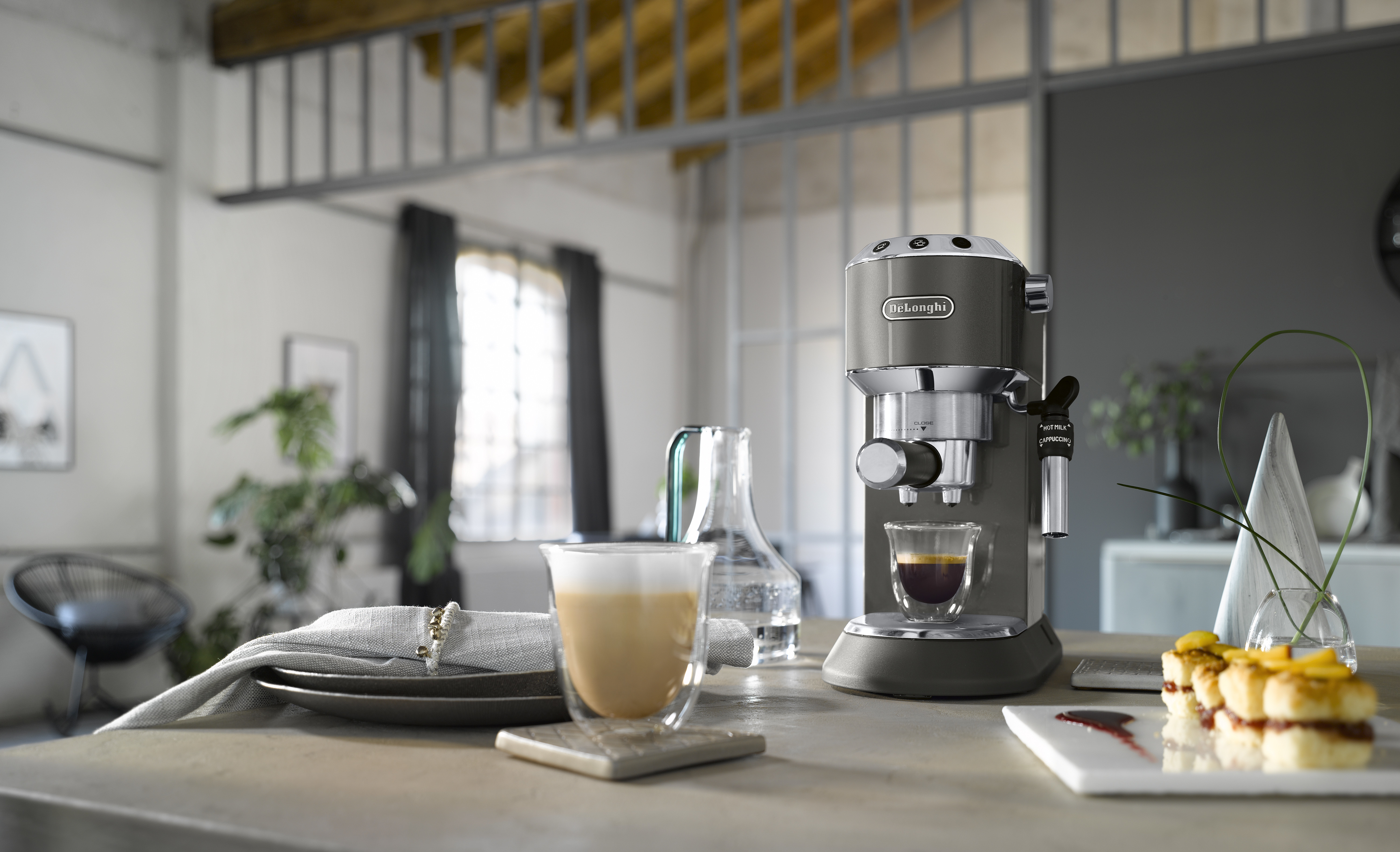 Máquina de espresso con dos vasos y pasteles sobre una mesa en interiores.