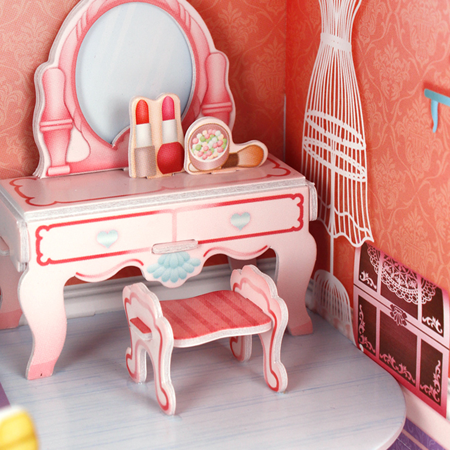 Un set da toeletta rosa in miniatura con specchio, trucco e uno sgabello, all'interno di una casa delle bambole.