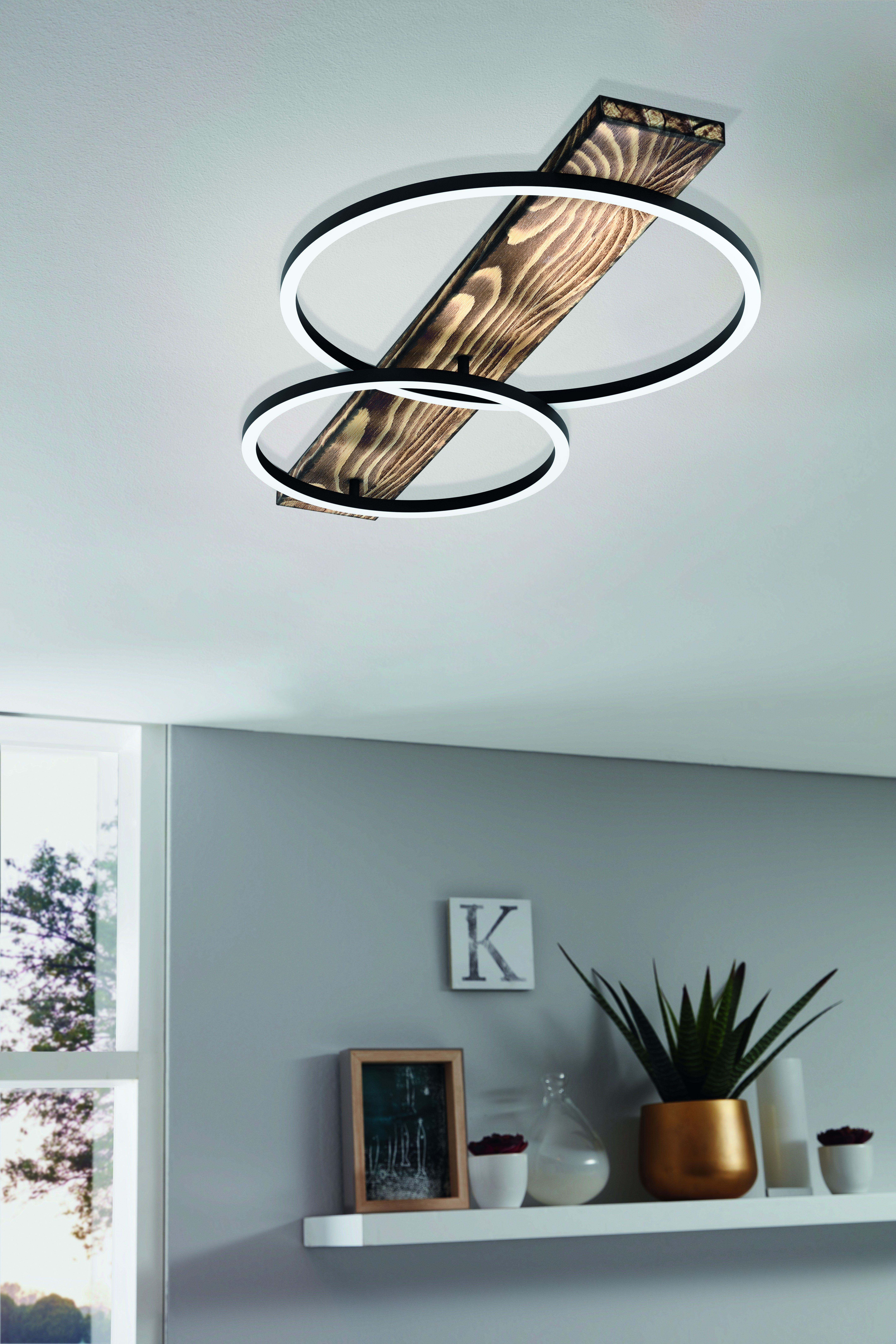 Deckenleuchte mit zwei Ringlichtern und einem Holzbalken. Weiße Decke und graue Wand.