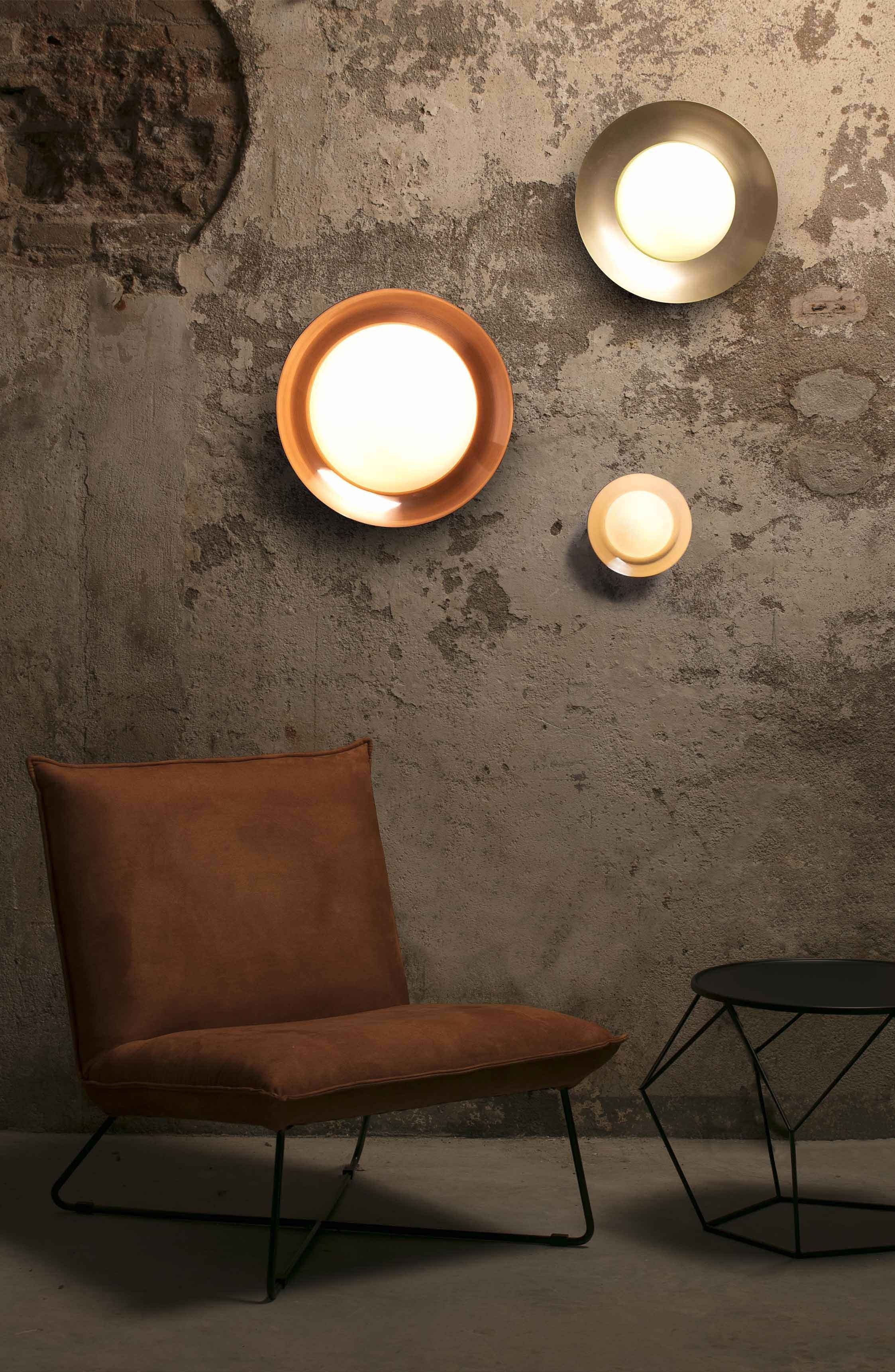 Drie ronde wandlampen op een getextureerde muur. Een stoel en een kleine tafel op de voorgrond.