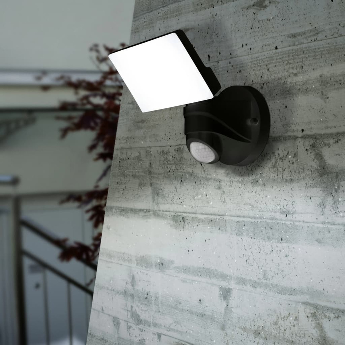 Ein schwarzer Flutlichtstrahler an einer Betonwand montiert. Das Licht ist an und der Hintergrund ist unscharf.