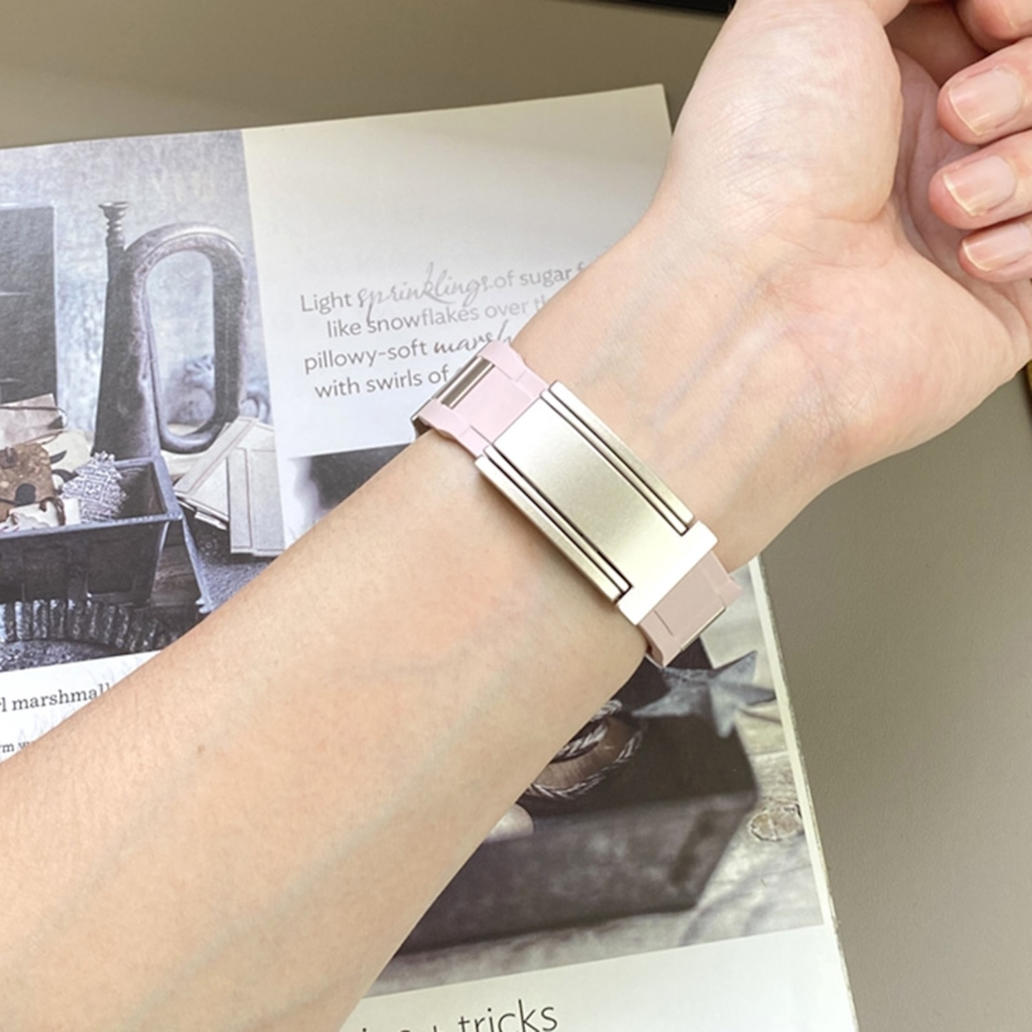 Ein Handgelenk mit einer goldenen und rosa Uhr. Die Uhr hat ein rechteckiges goldenes Zifferblatt und ein rosa Armband.