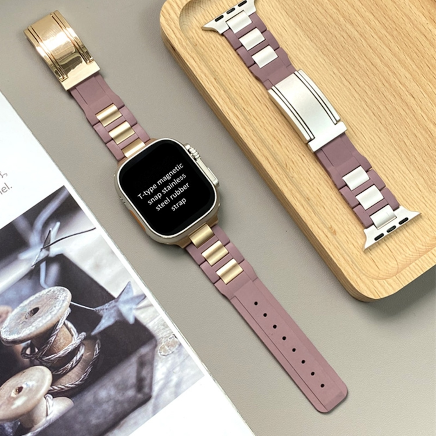 Apple Watch mit rosa und goldenem Armband, auf einem Holztablett ausgestellt.