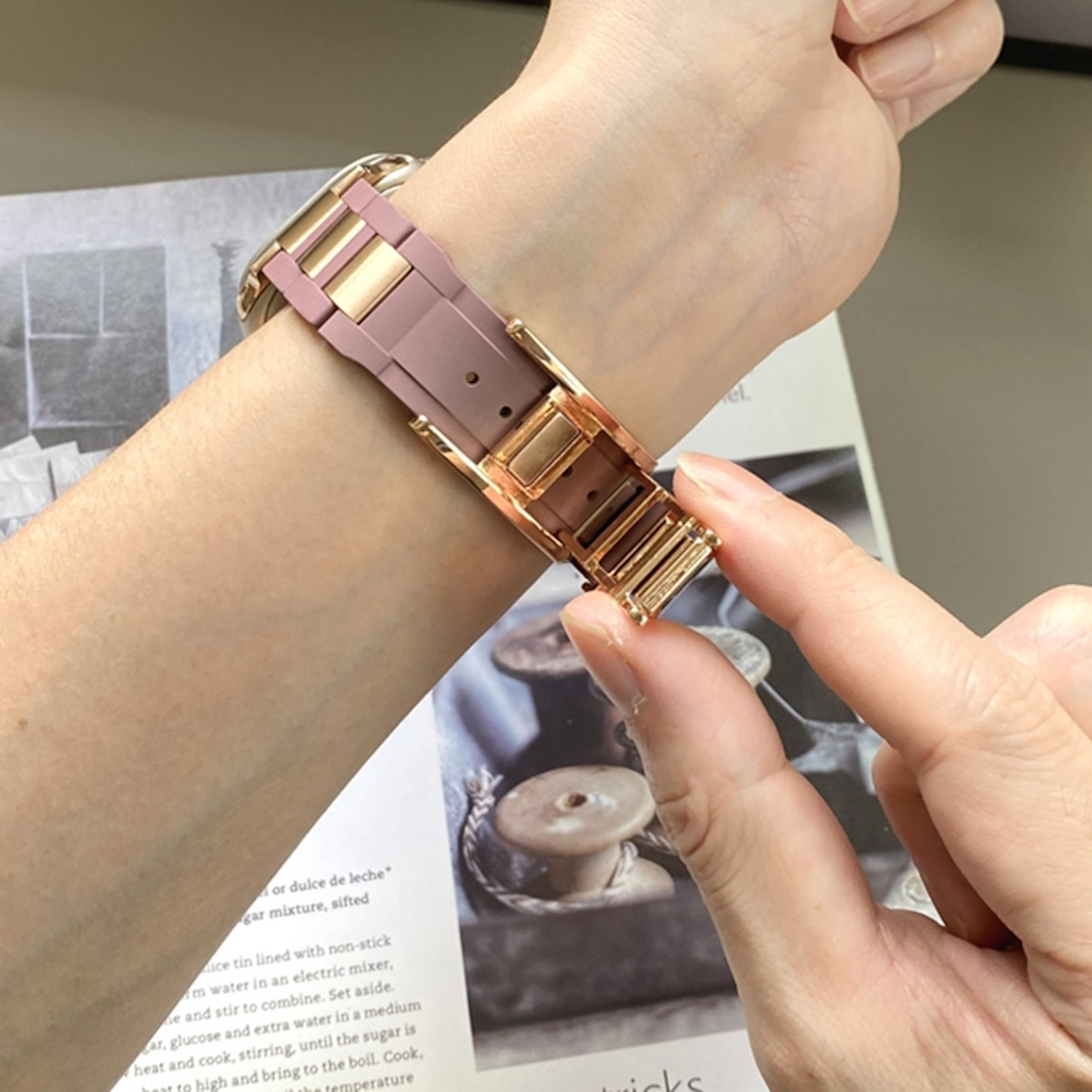 Handgelenk einer Person mit einer Uhr mit pinkfarbenem Armband und goldenen Akzenten.
