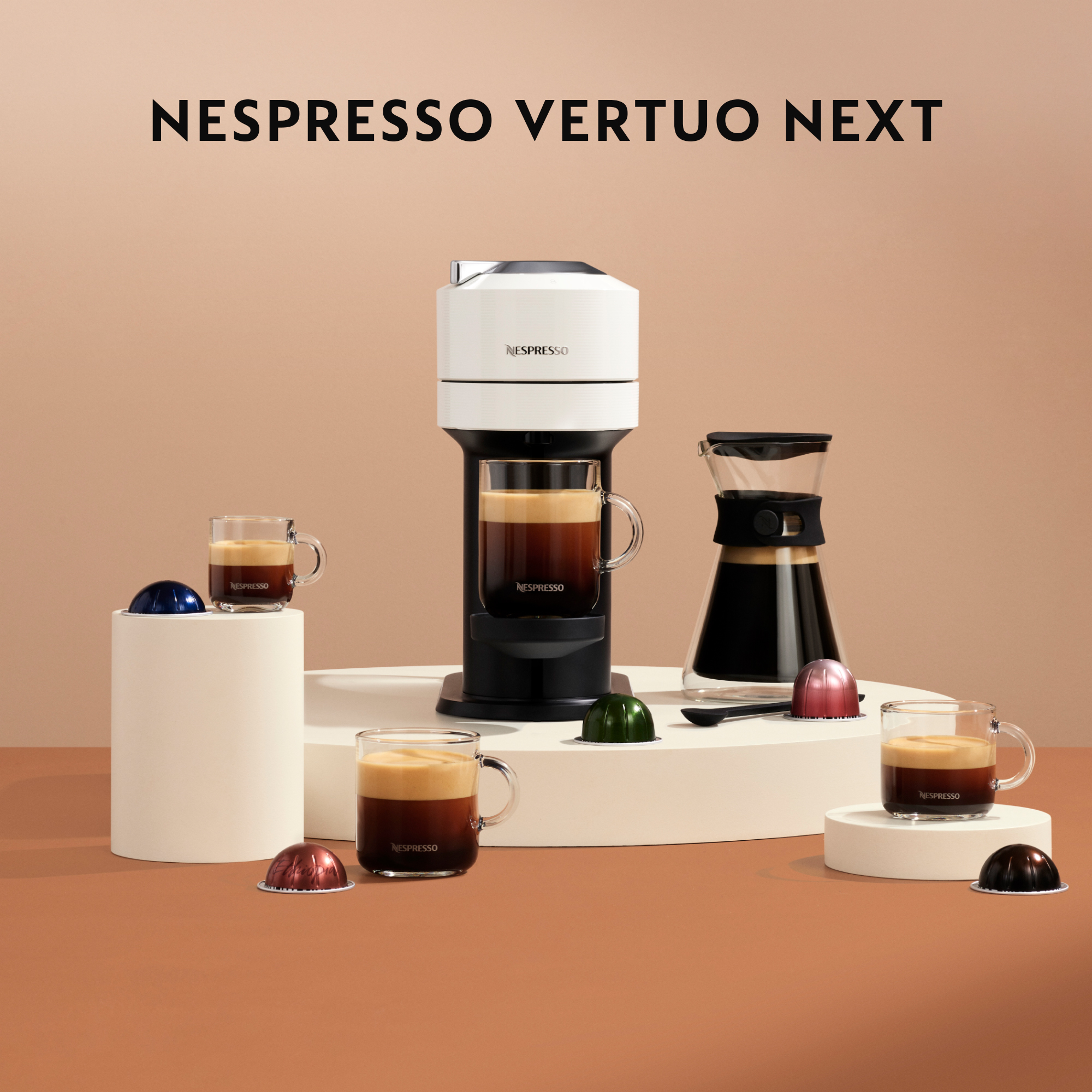 Cafetera Nespresso Vertuo Next con tazas de café, cápsulas y una jarra.