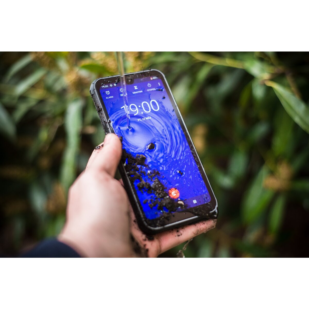 Eine Hand hält ein blaues Smartphone mit blauem und schwarzem Bildschirm. Der Bildschirm zeigt die Zeit und Schmutz.