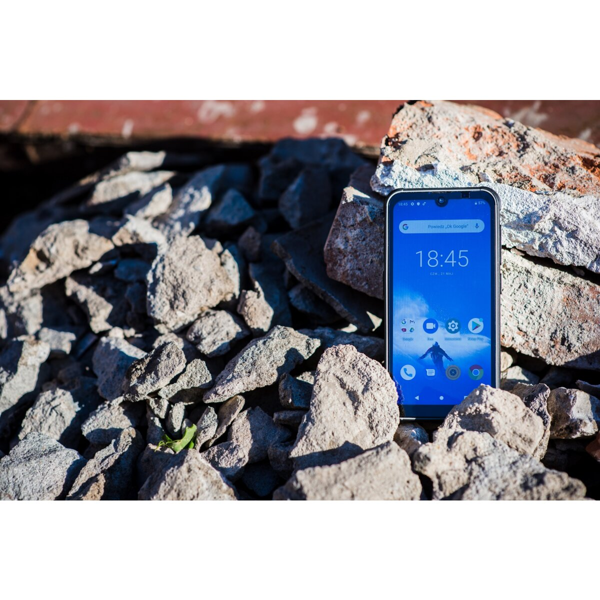 Ein Smartphone liegt auf Felsen. Der Bildschirm zeigt eine blaue Oberfläche mit der Uhrzeit 18:45.