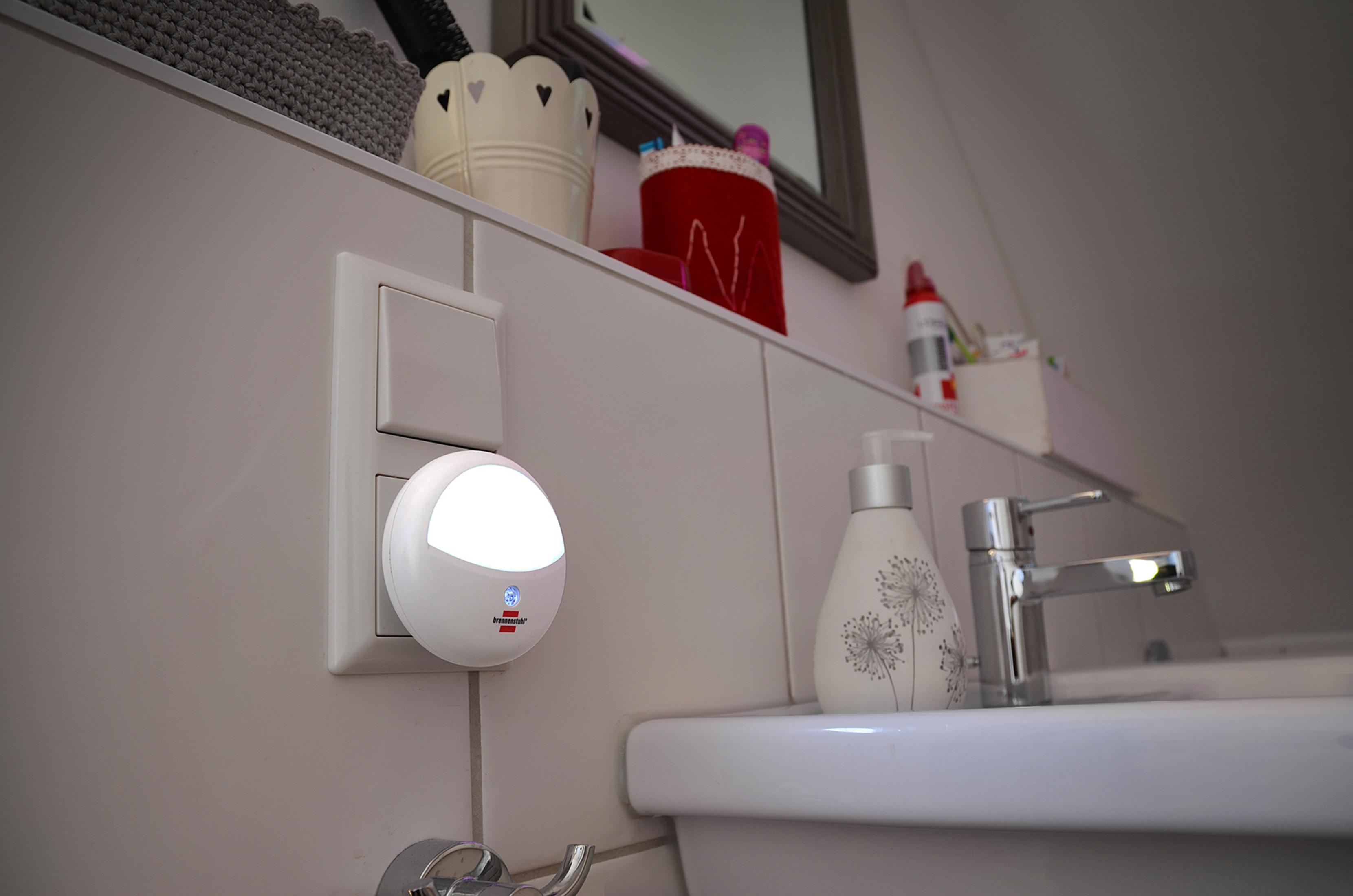 A white night light plugged into a wall outlet. The light is on, and the wall is white.