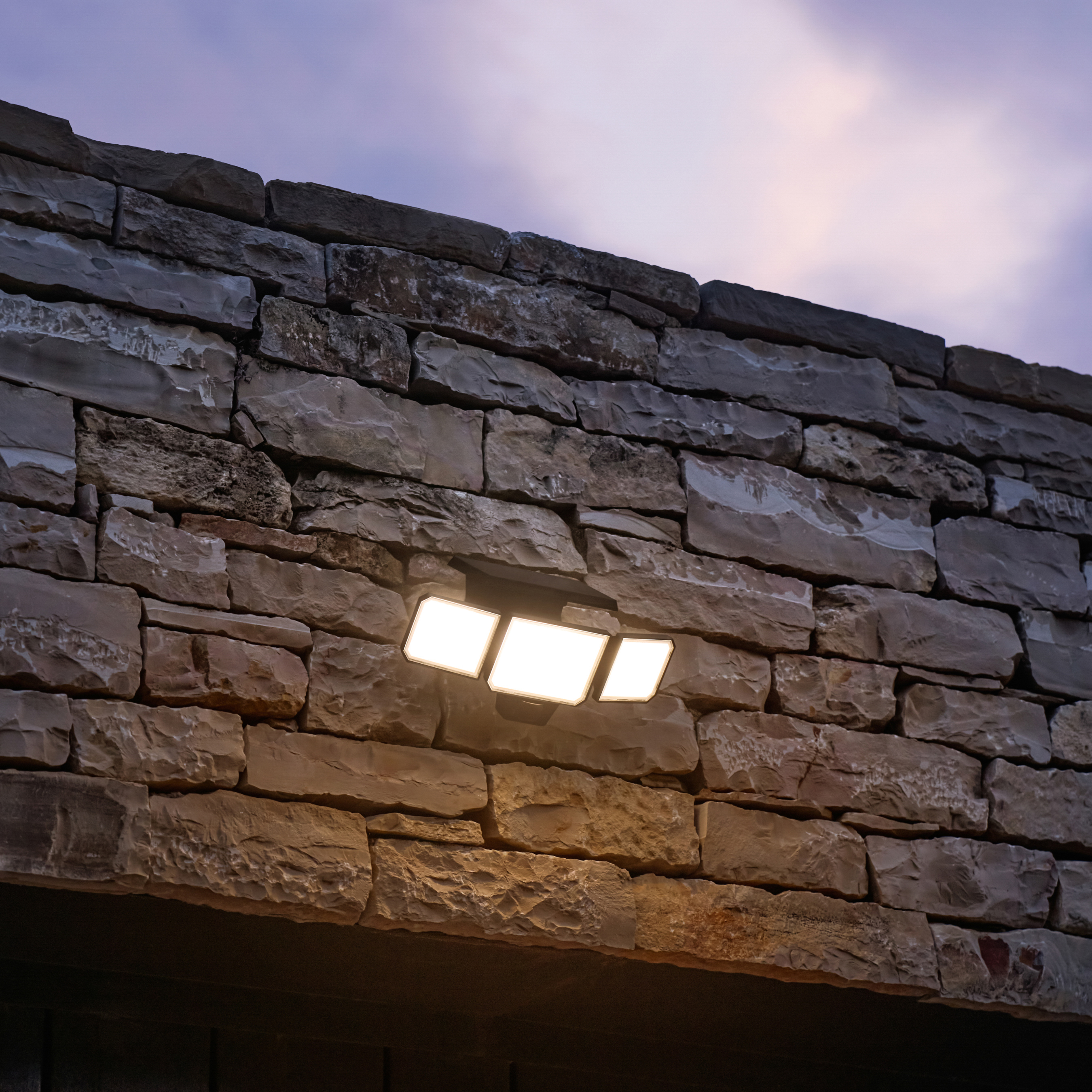 Tre luci LED montate su un muro di pietra, che illuminano la superficie strutturata.