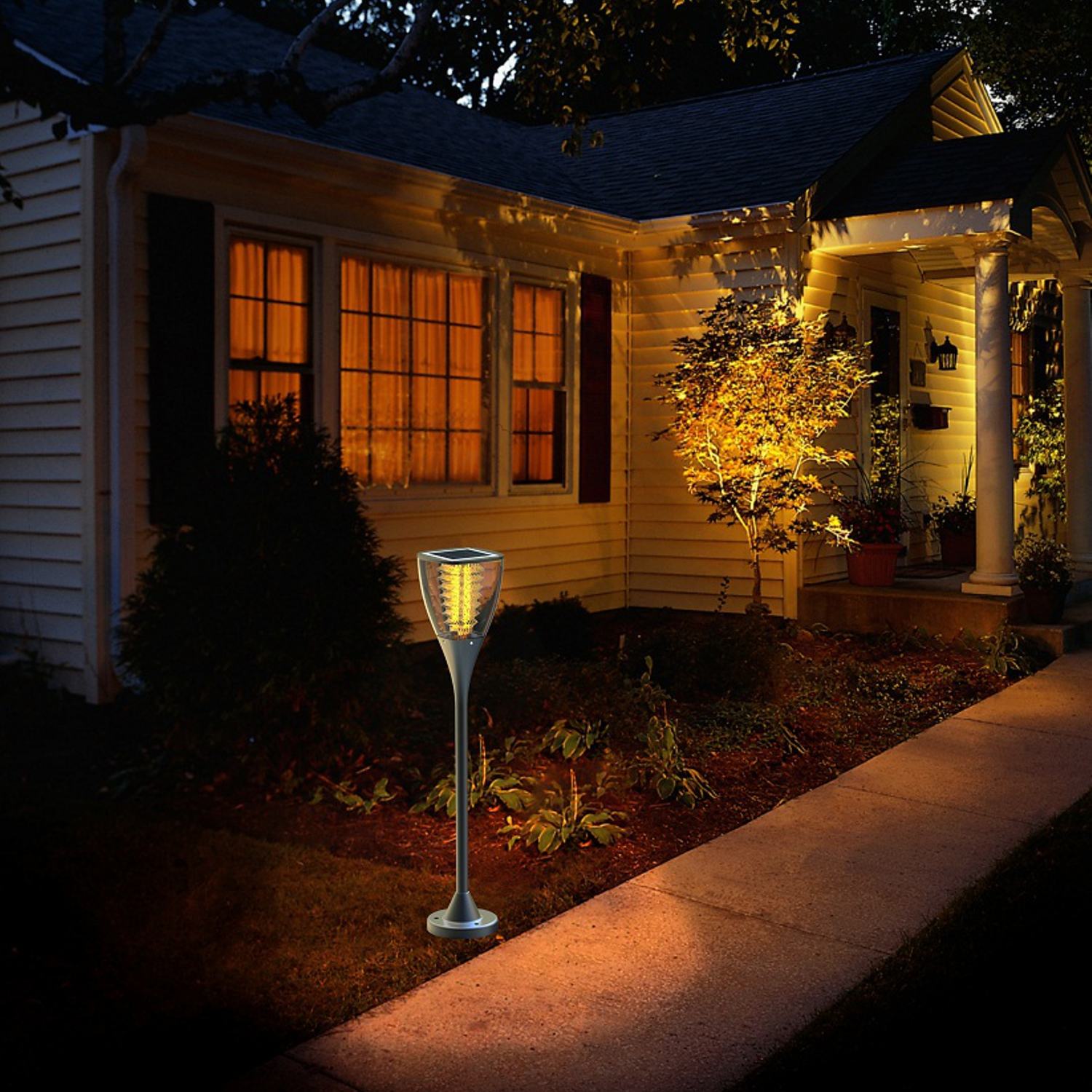 Una luce da giardino a energia solare di fronte a una casa di notte. La luce ha un paletto.