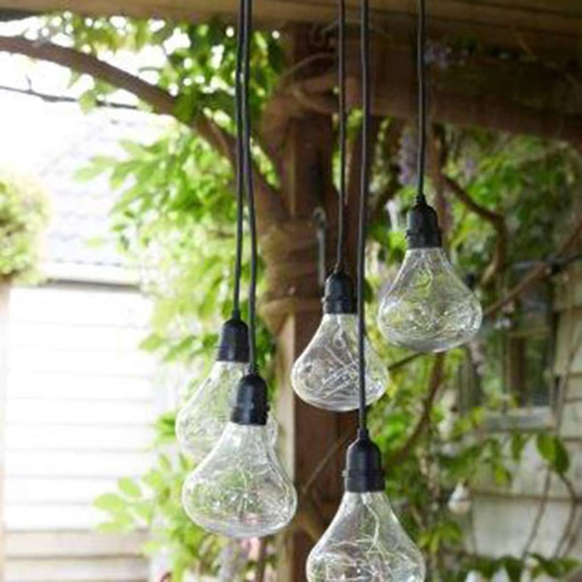Bombillas colgantes, cristal transparente, con cables, en un jardín, de día.