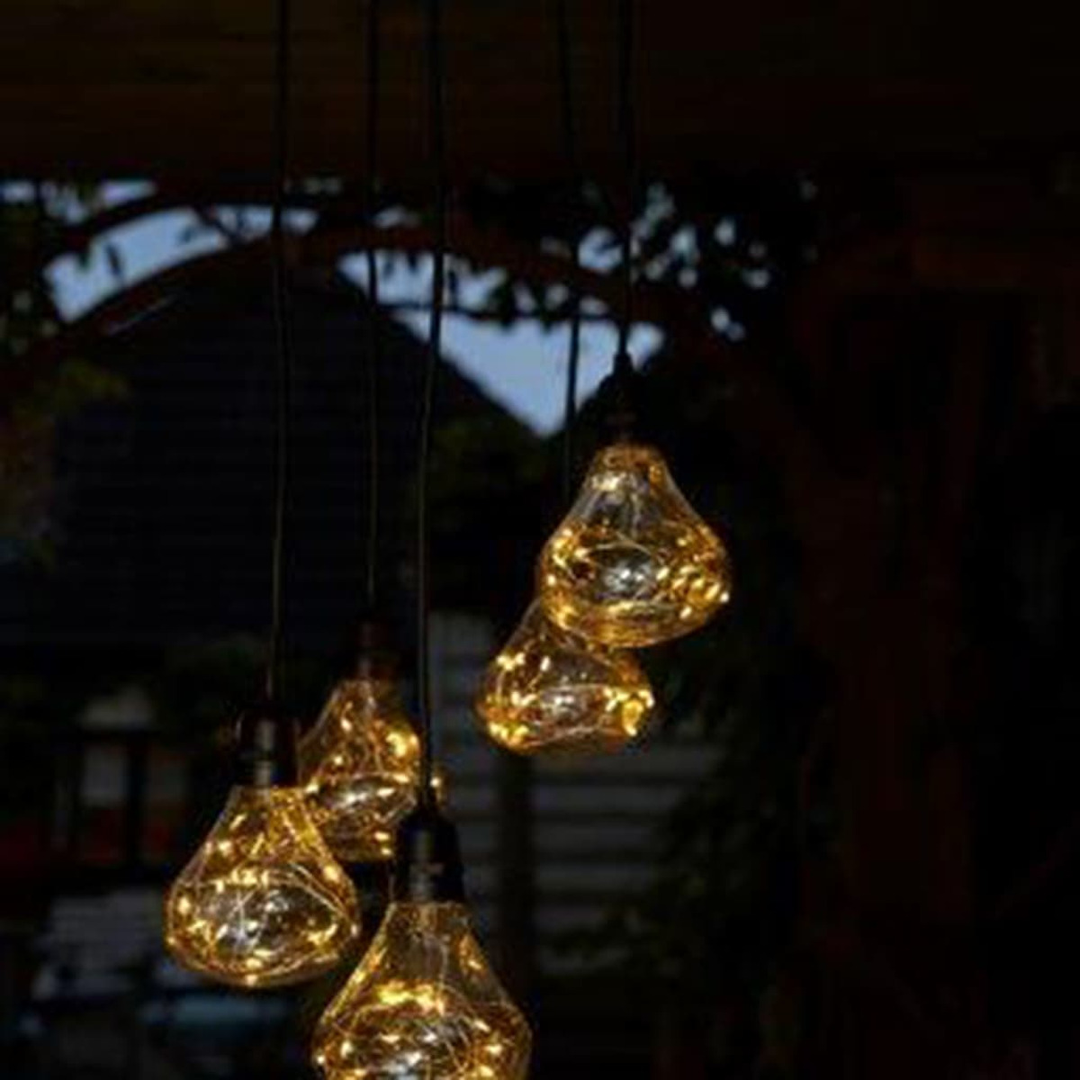 Cadena de luces colgantes con bombillas transparentes en forma de lágrima. Las luces están encendidas, en un ambiente oscuro.