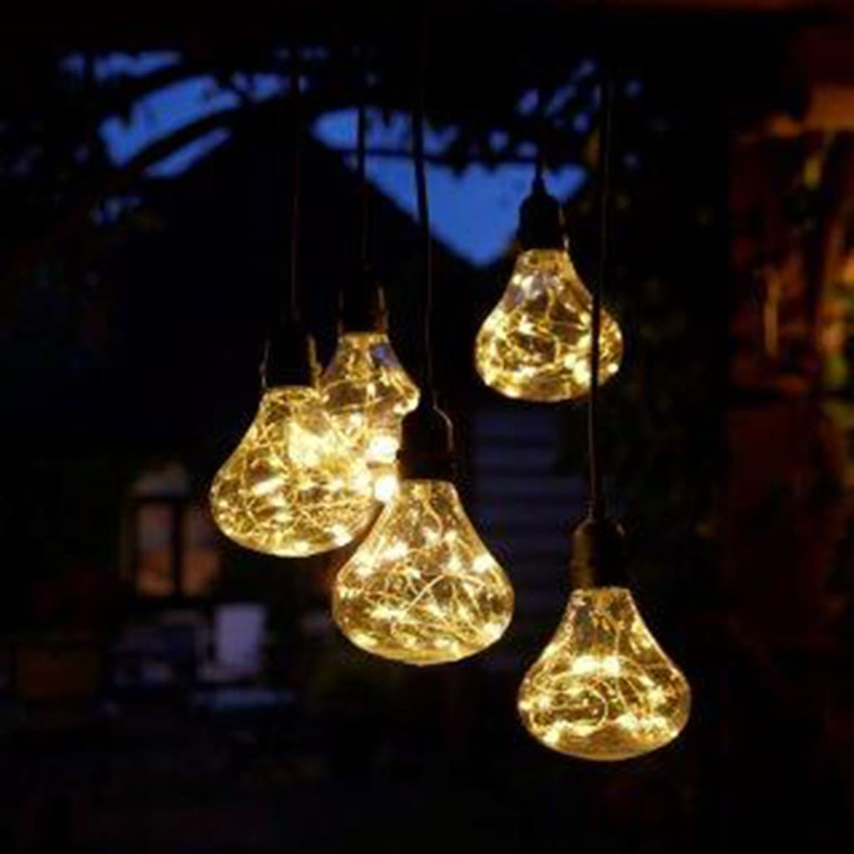 Cinco bombillas colgantes en forma de lágrima, brillantes, con luces de cadena dentro, en la oscuridad.