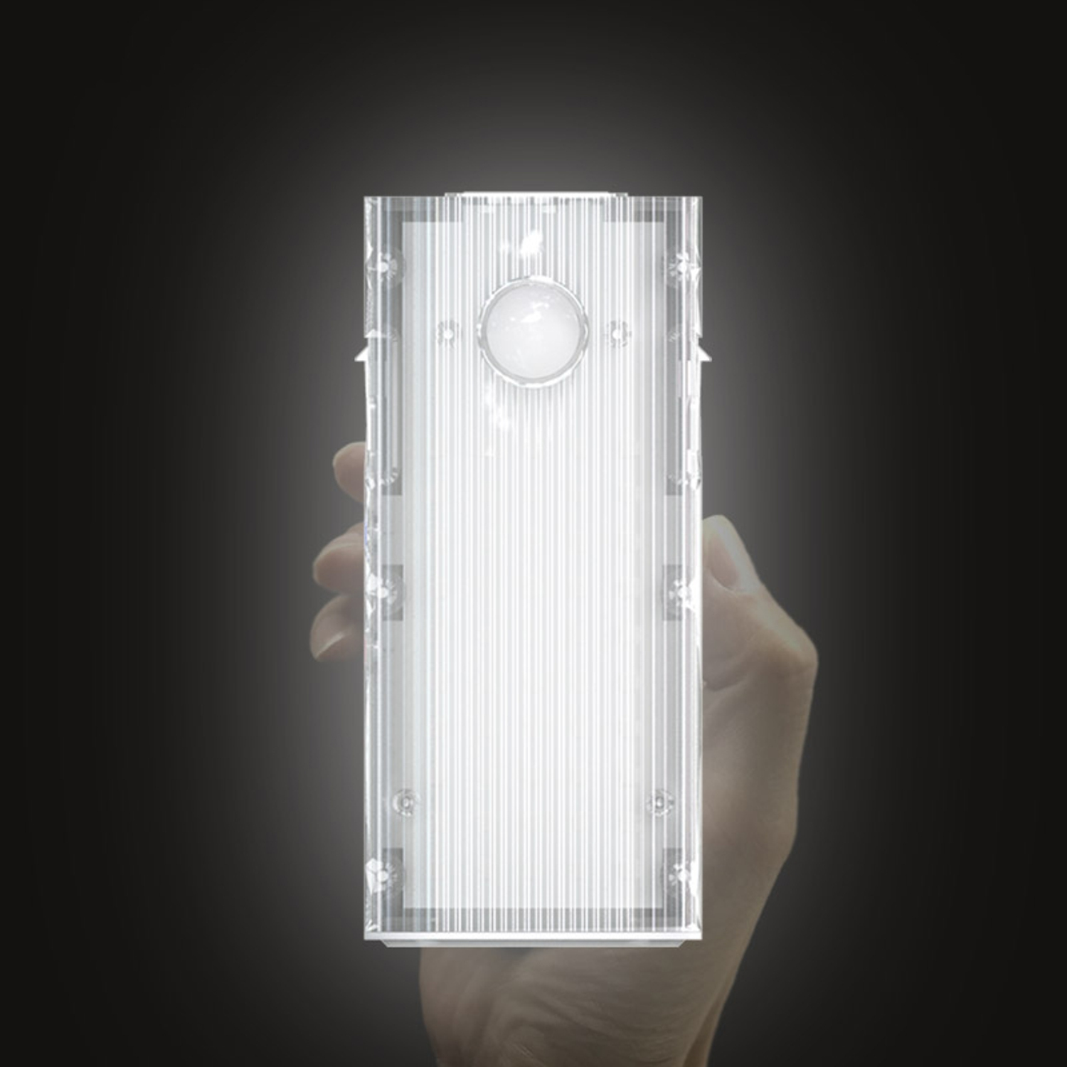 A hand holding a transparent rectangular light. The light is on and emits a bright white light.