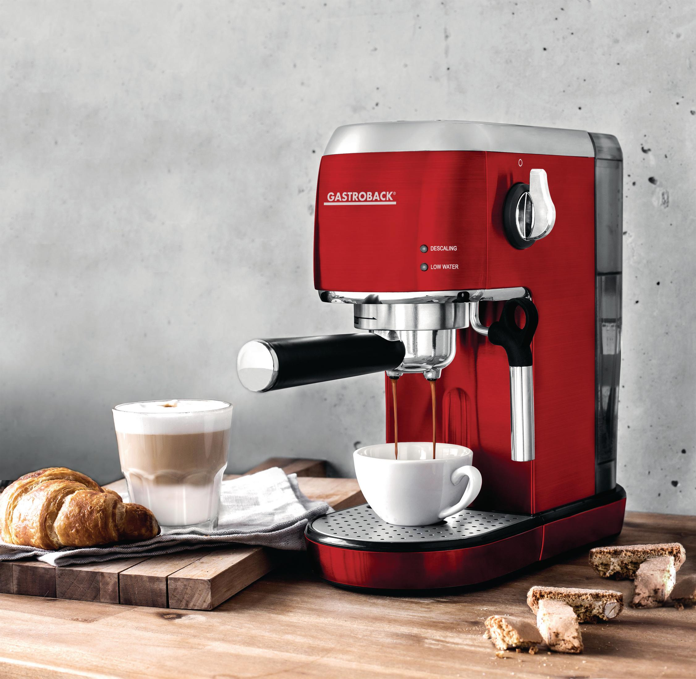 Czerwony ekspres do kawy z kawą wlewaną do białego kubka. Rogalik i ciasteczka na stole.