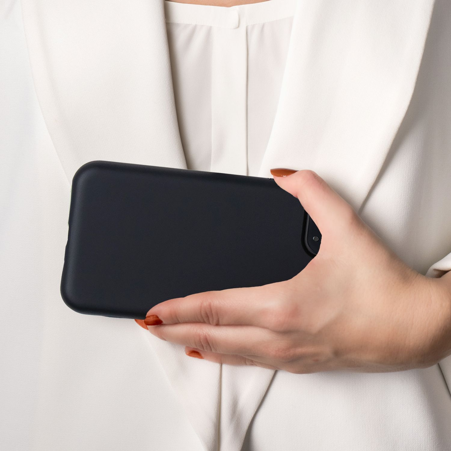 Eine Person mit weißem Blazer hält ein schwarzes Telefon, der Bildschirm ist nicht sichtbar.