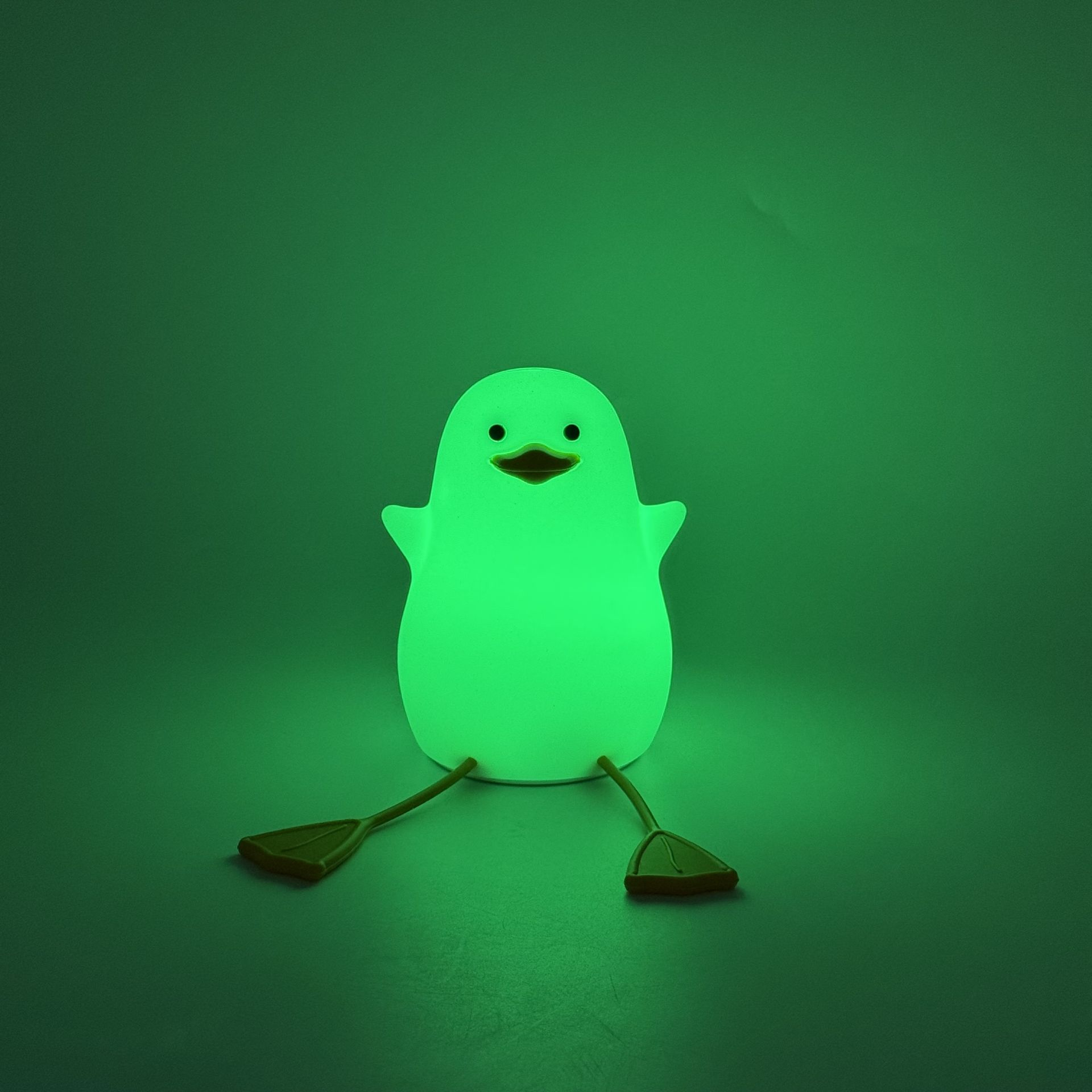 Lampada ad anatra verde in una stanza illuminata di verde. Ha zampe e un viso sorridente.
