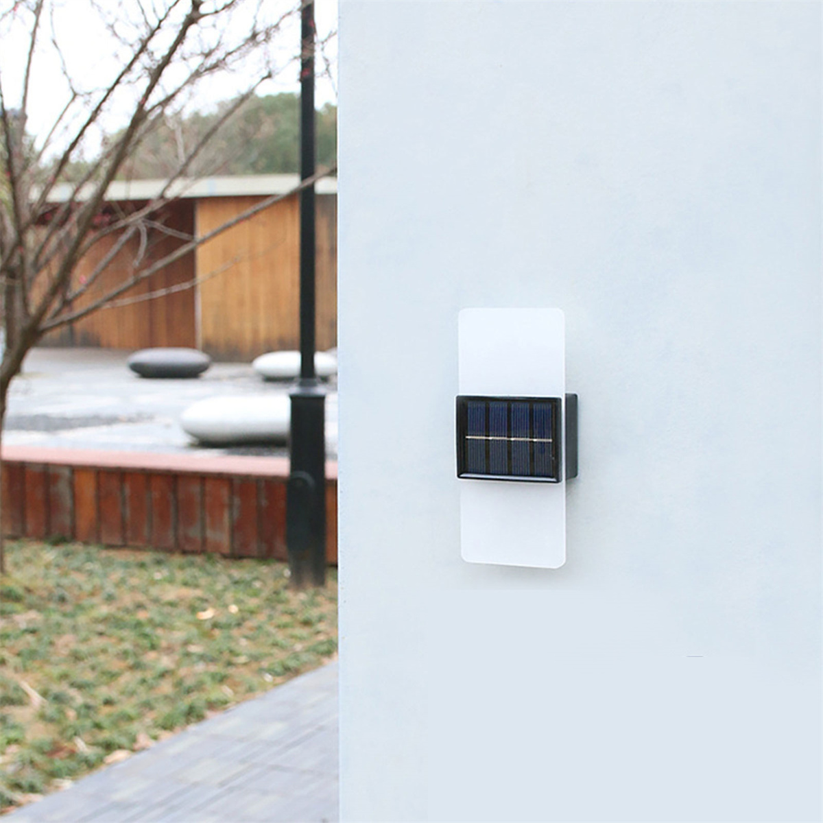 Solarbetriebene Wandleuchte an einer weißen Wand, mit Park und Bäumen im Hintergrund.