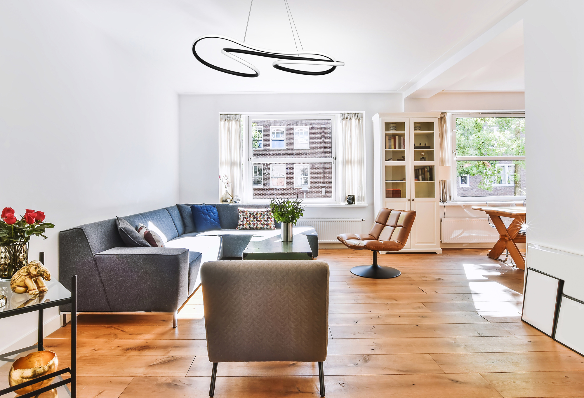 Salón moderno con sofá gris, suelo de madera y una lámpara de techo única.