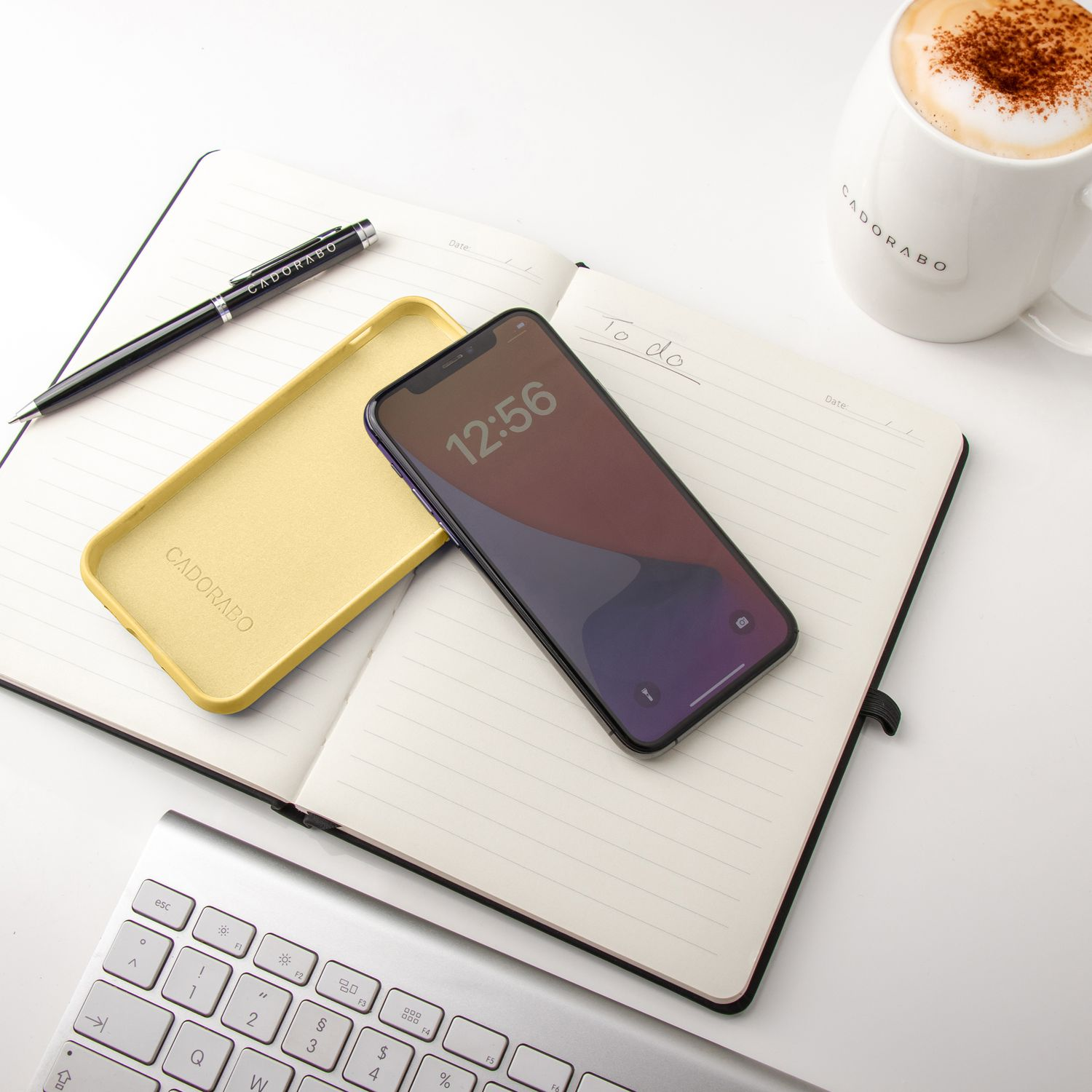 Ein Telefon, seine Hülle, ein Stift und ein Notizbuch auf einem weißen Schreibtisch.