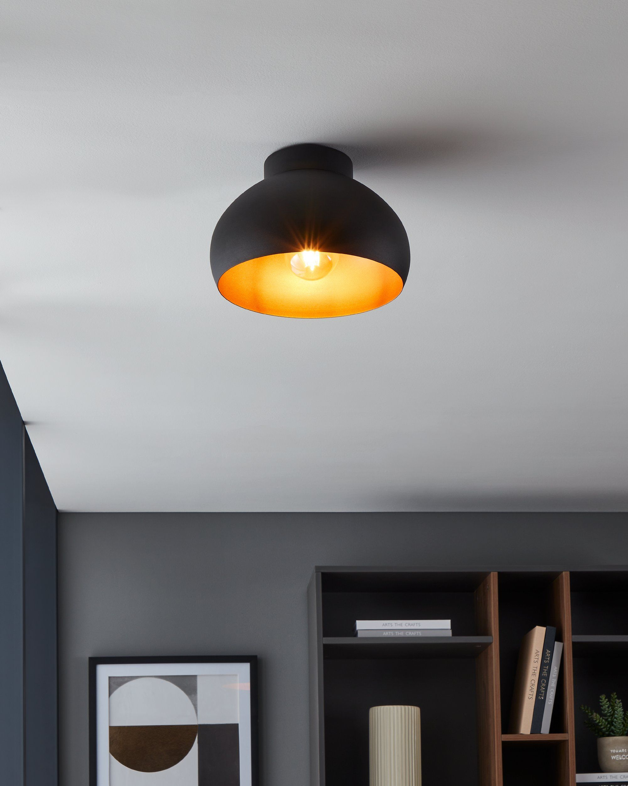 Lampada da soffitto nera con interno dorato e lampadina visibile.