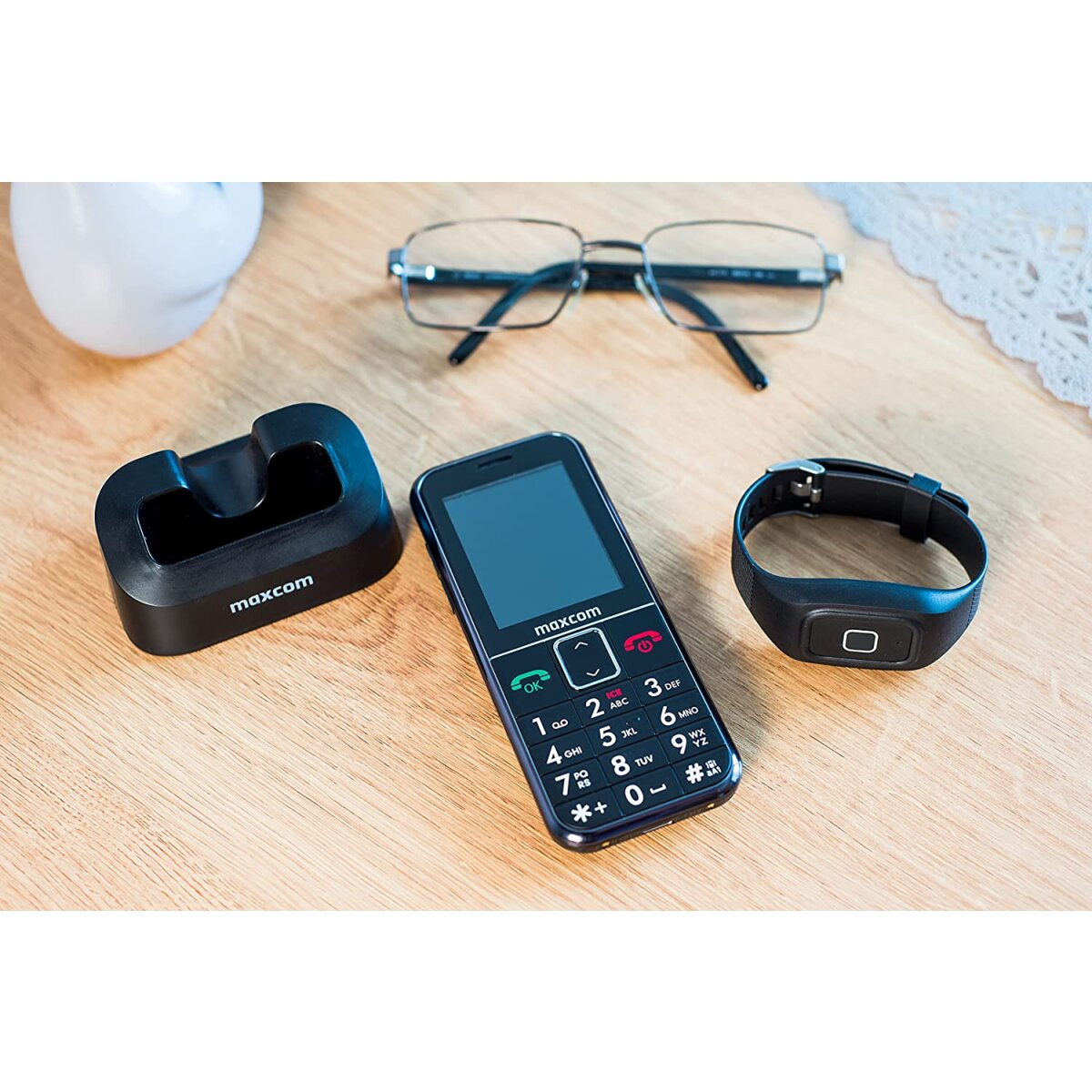 Teléfono inteligente con cargador, pulsera inteligente y gafas sobre una mesa de madera.
